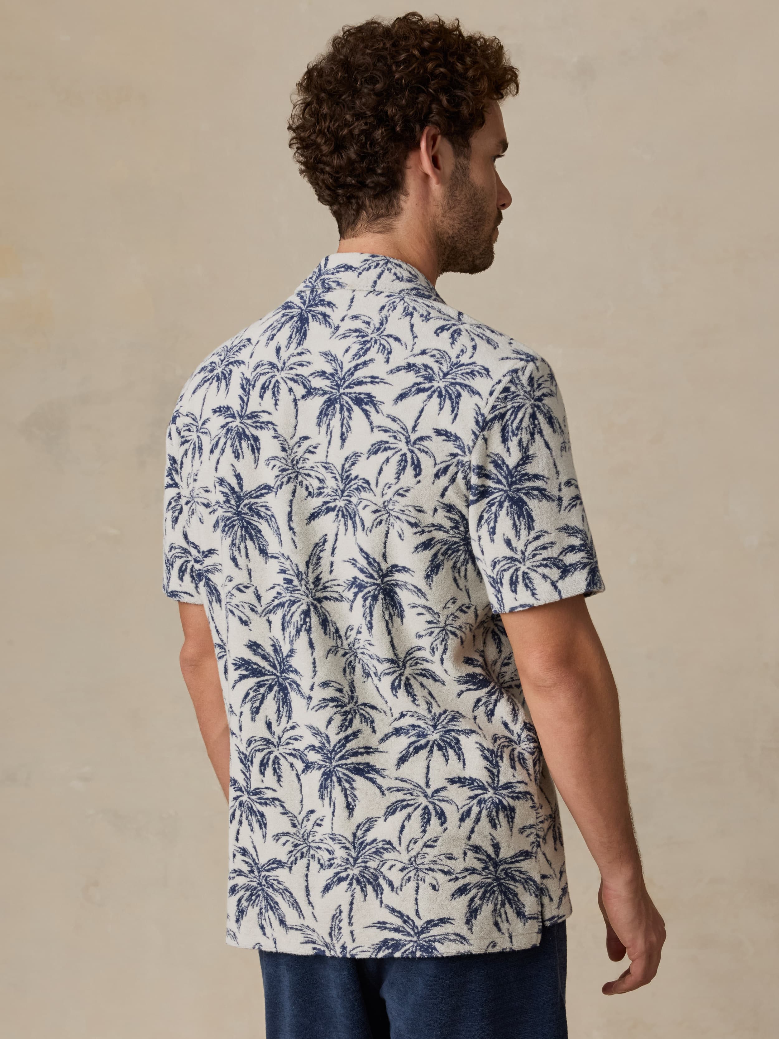 Man wearing a white shirt with blue palm tree pattern against a beige background