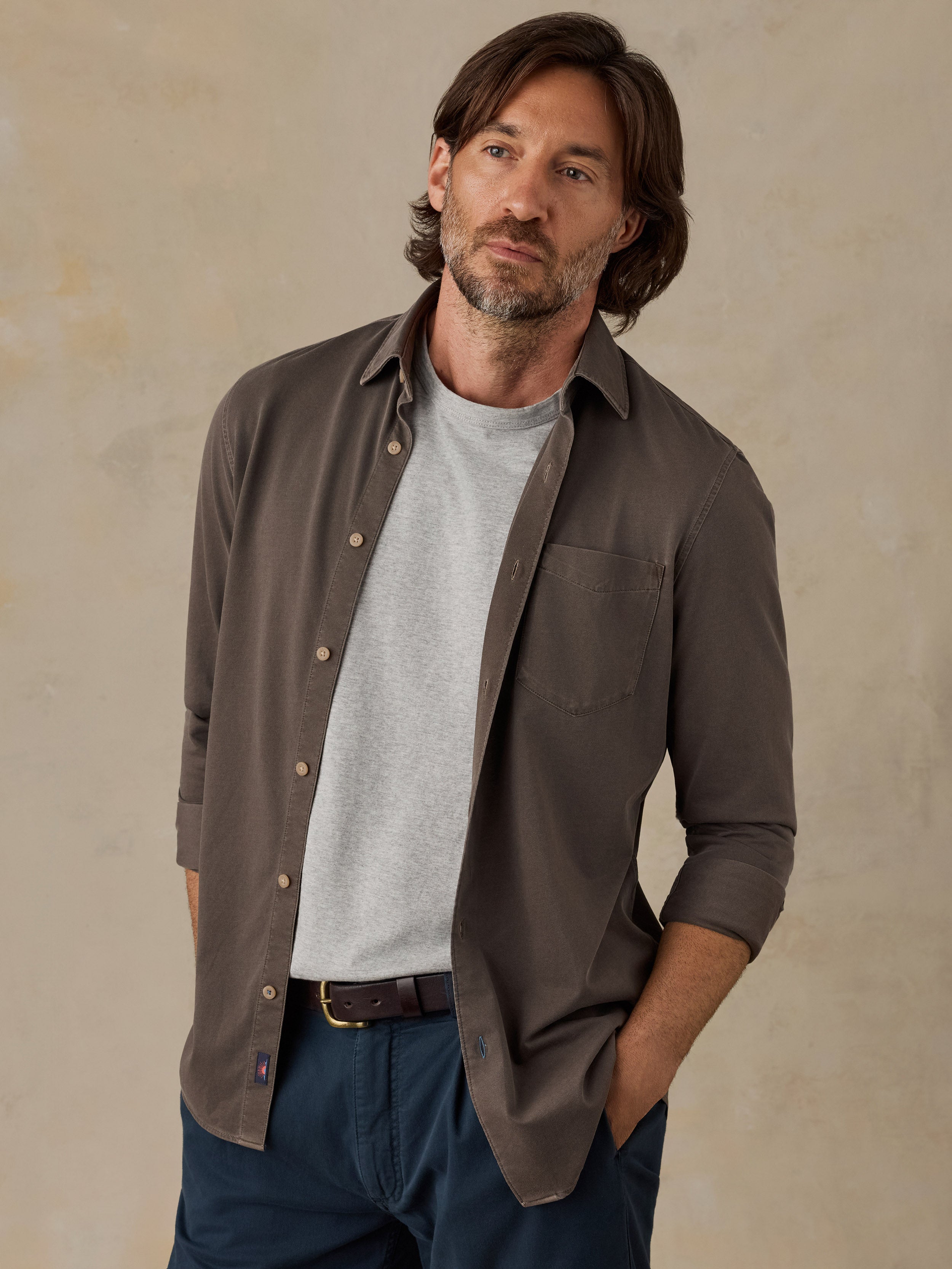 Man wearing a brown button down shirt and navy chino pants against a beige background