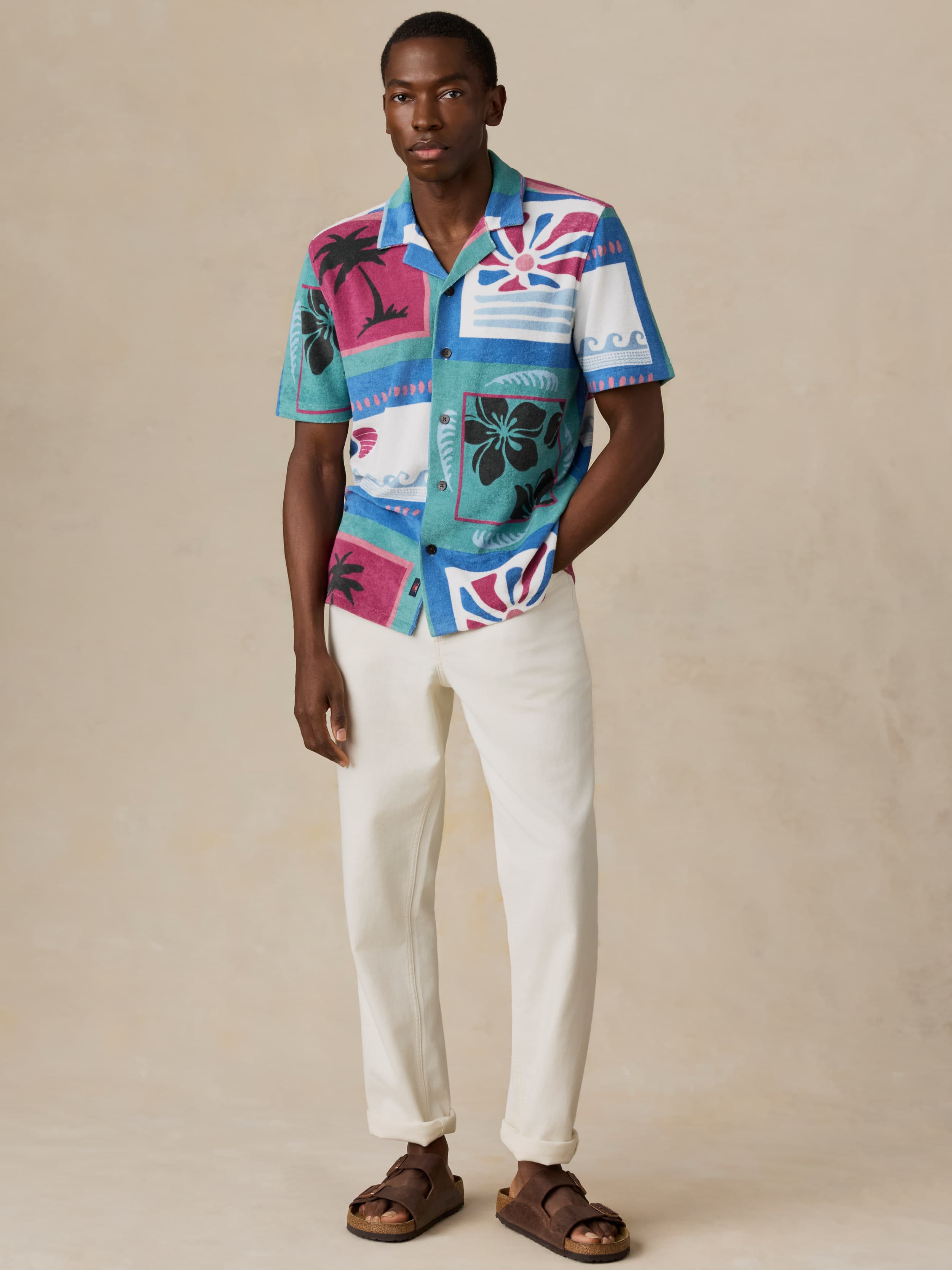Man wearing a colorful patterned shirt and white pants on a beige background