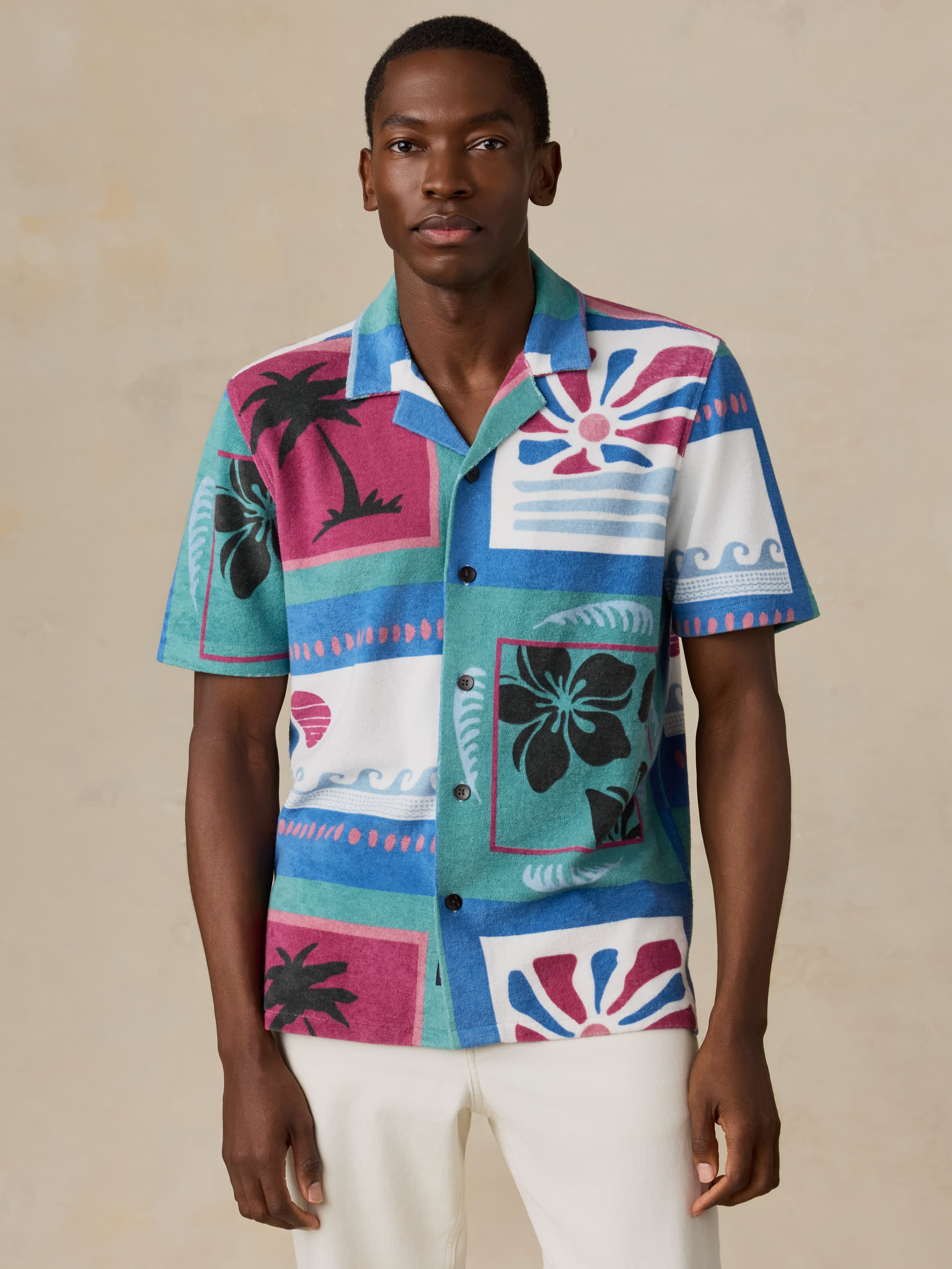 Man wearing a colorful patterned shirt with palm trees and abstract designs on a beige background