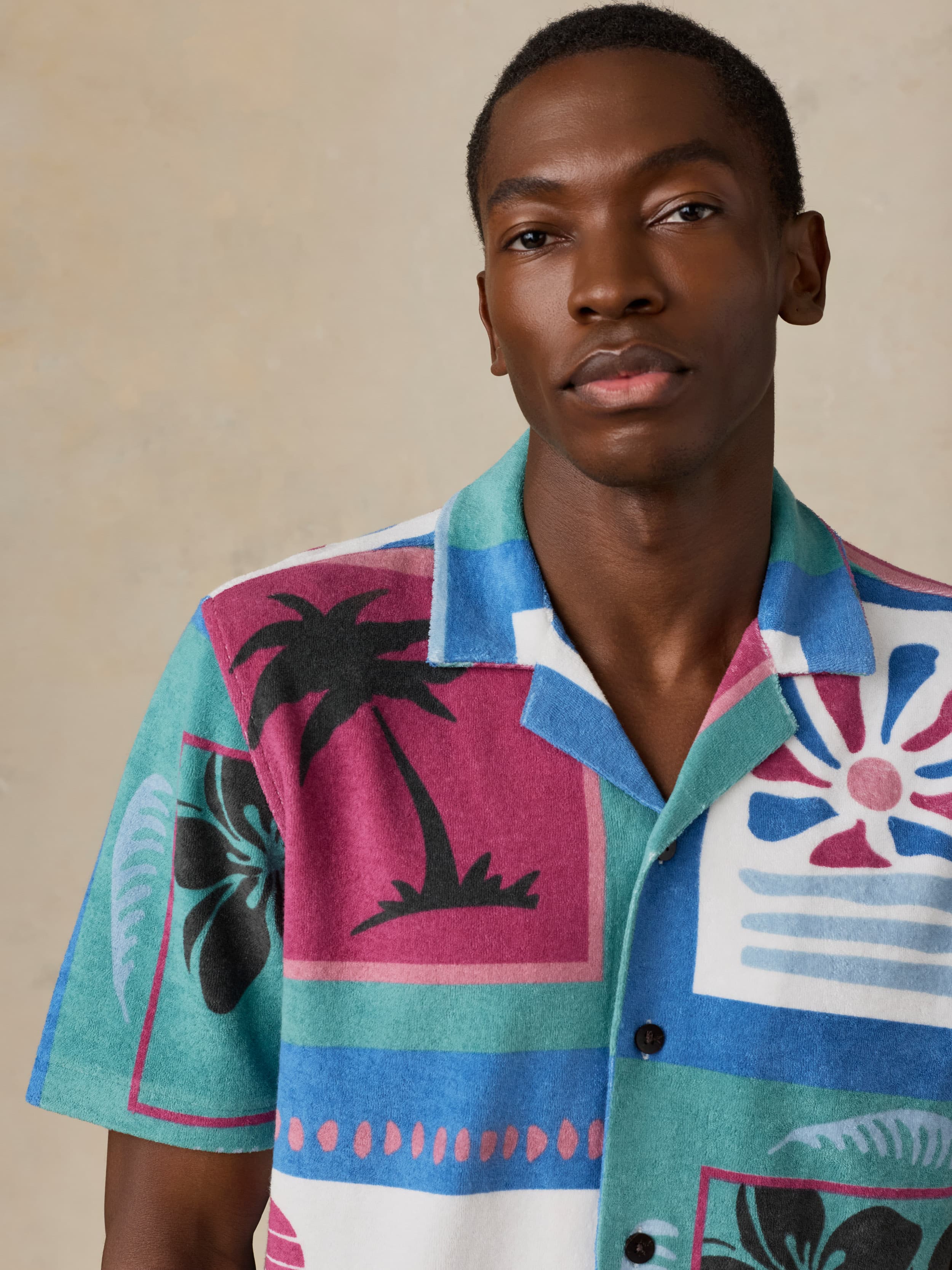 Man wearing a colorful patterned shirt with palm tree design against a beige background