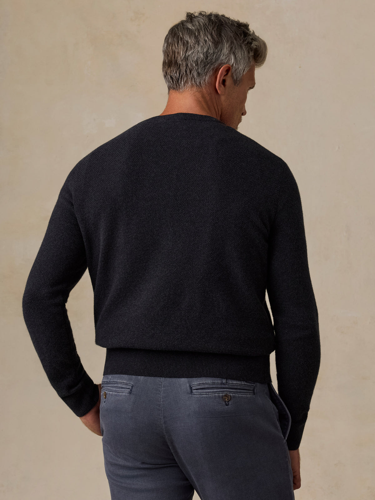 A man viewed from behind wearing a dark charcoal knit sweater and slate blue trousers, image 4 of 7