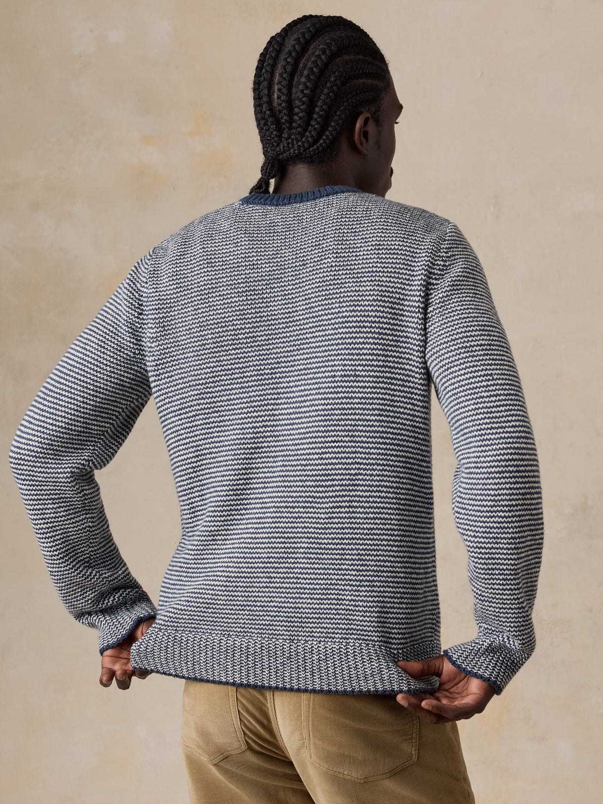A man viewed from behind wearing a blue striped sweater and tan corduroy pants, image 2 of 5