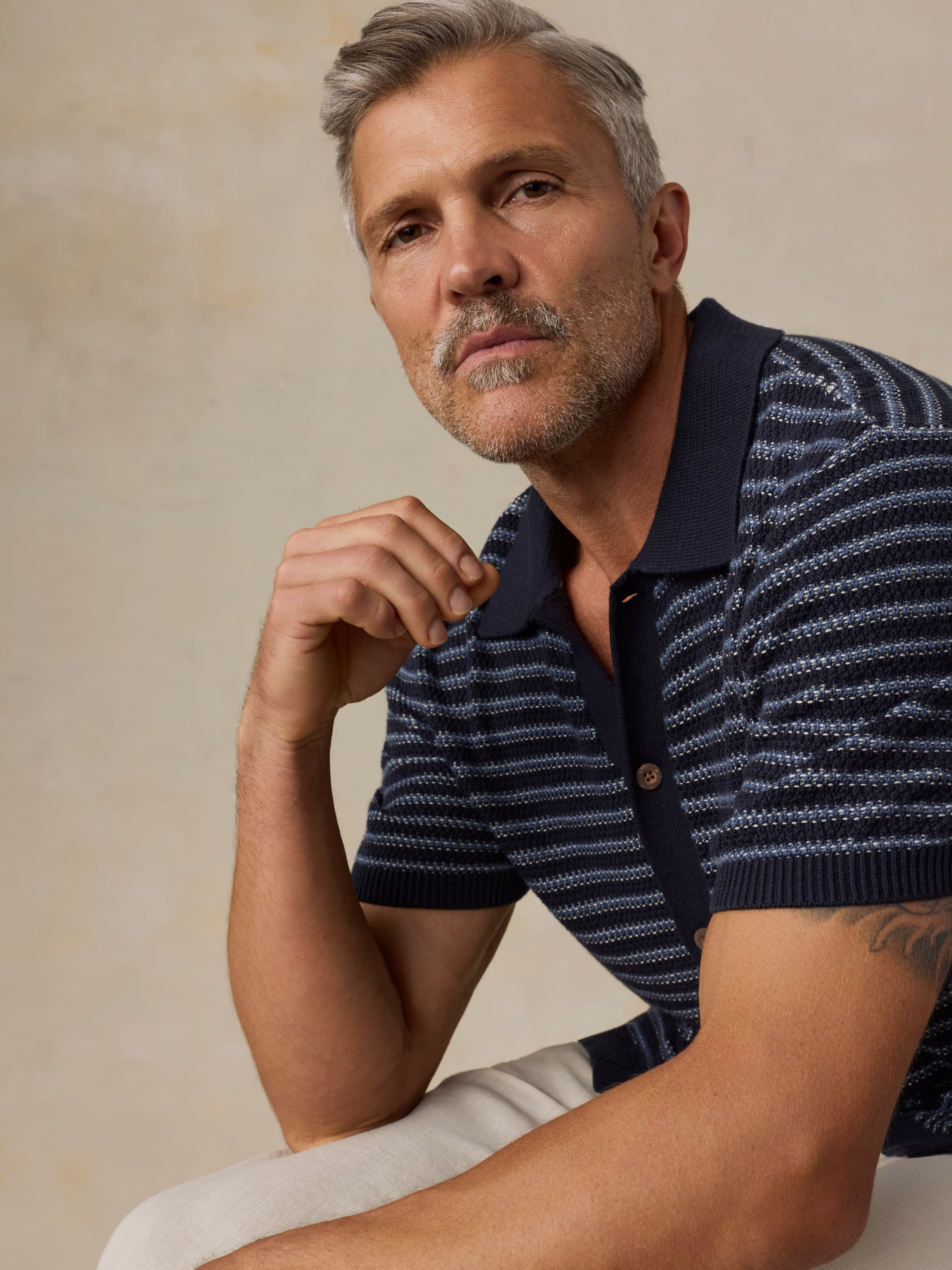 Man wearing a navy striped polo shirt against a beige background