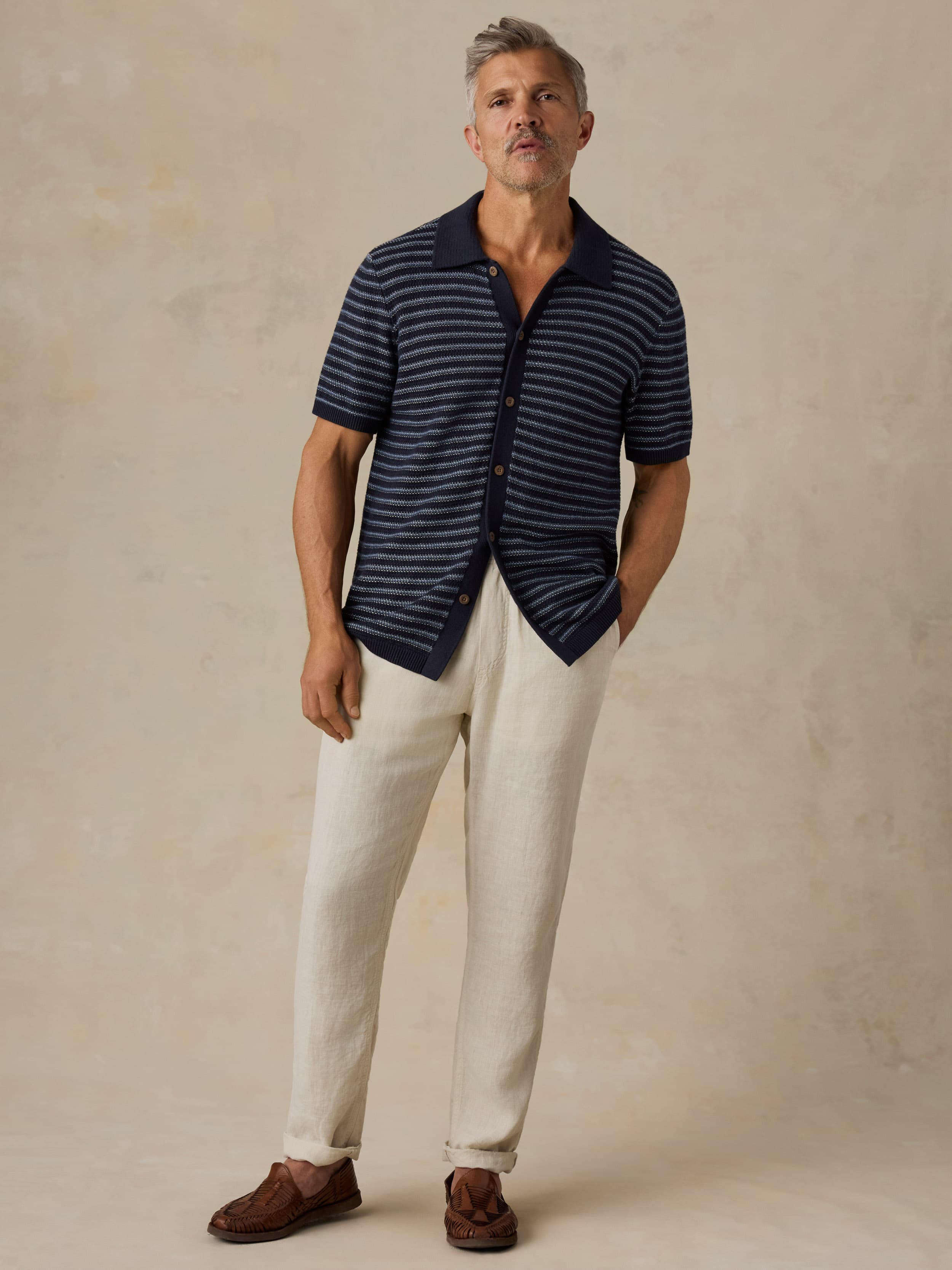 Man wearing a striped shirt and white pants against a beige background