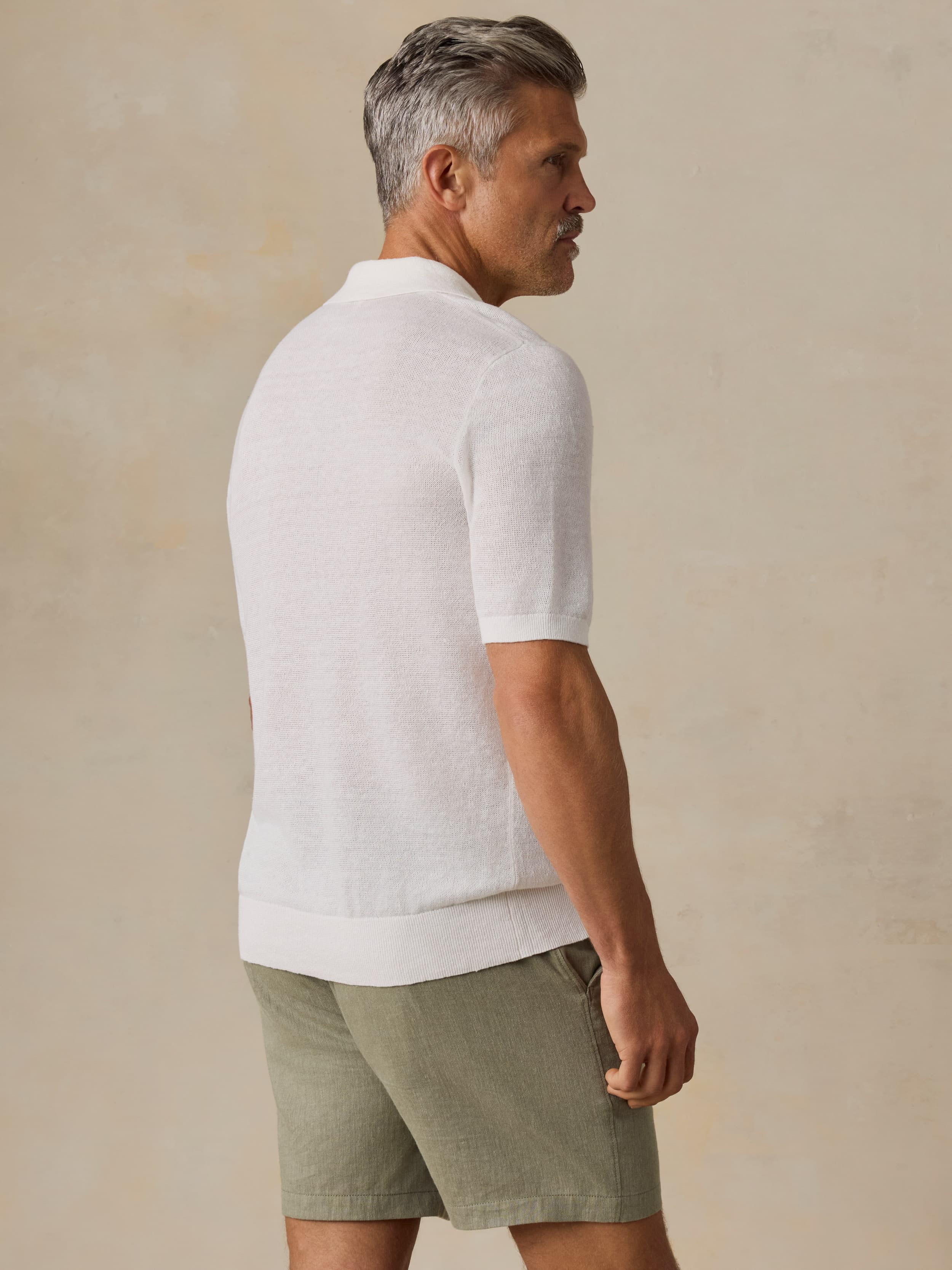 Man wearing a white polo shirt and green shorts against a beige background