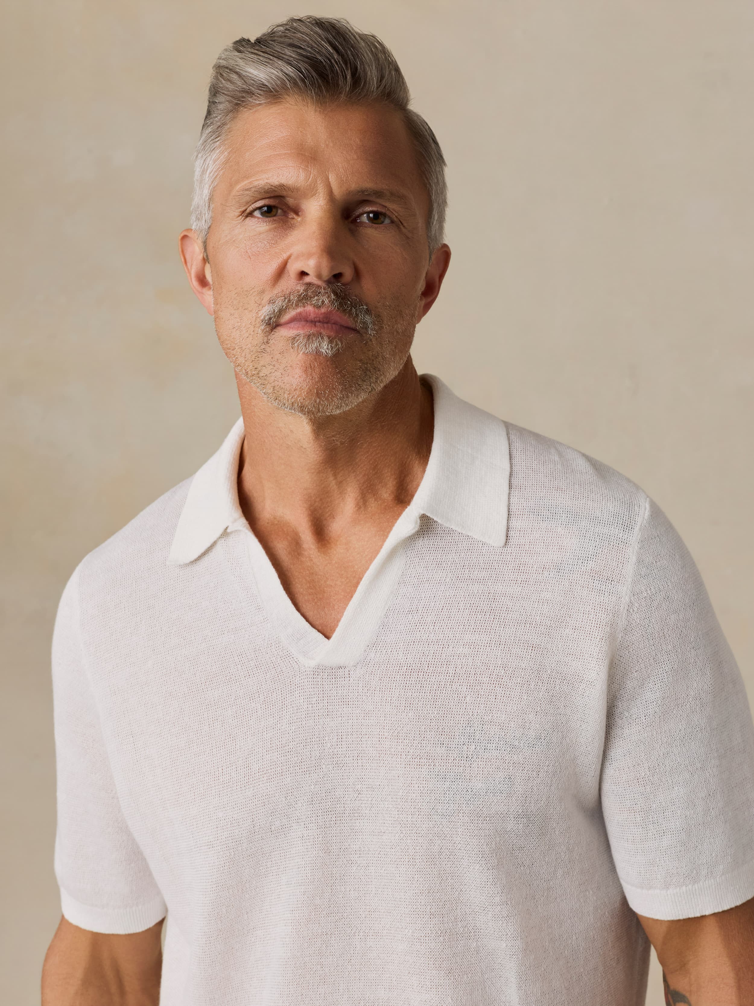 Man wearing a white polo shirt against a beige background