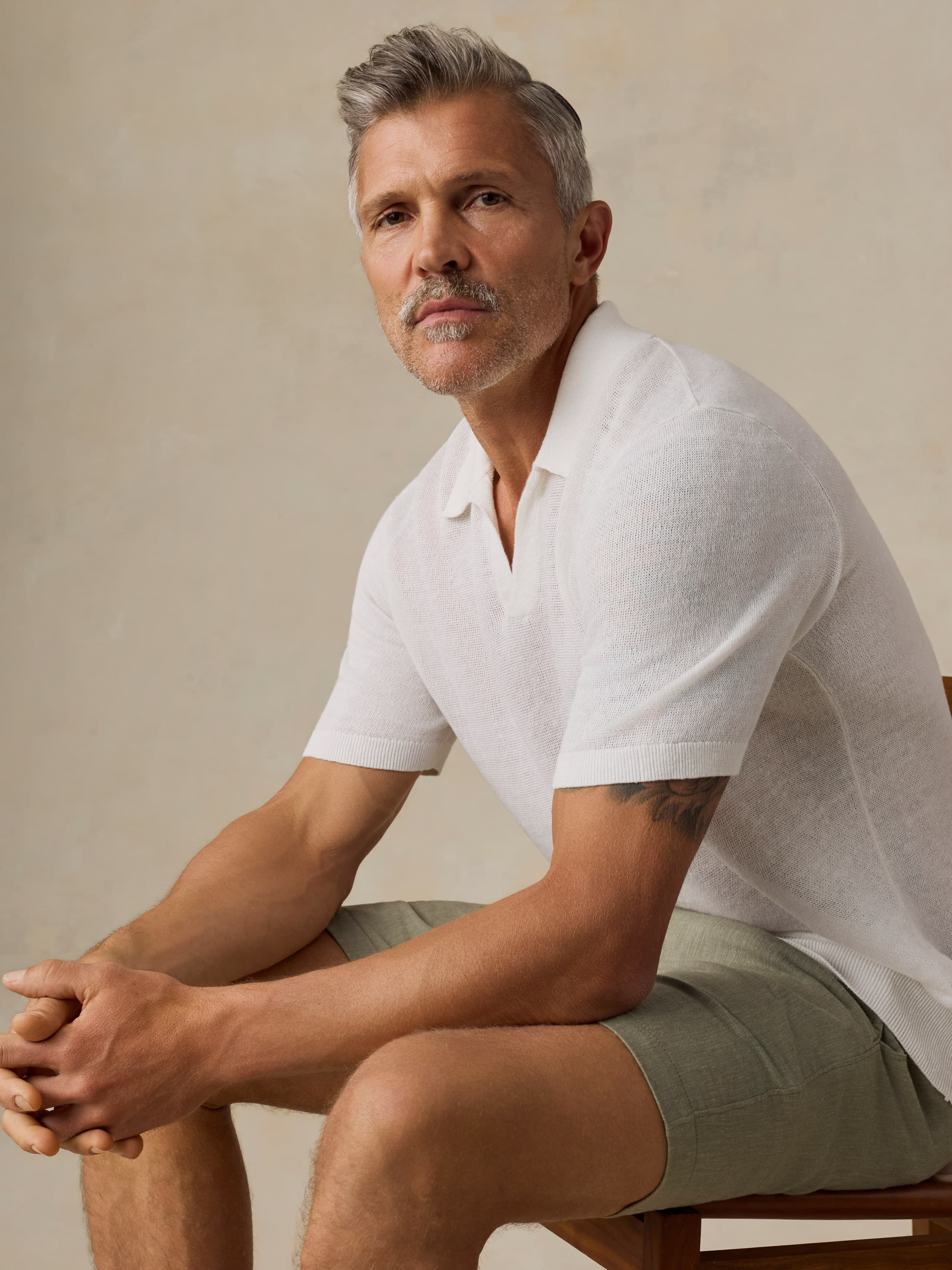 Man wearing a white polo shirt and green shorts against a beige background