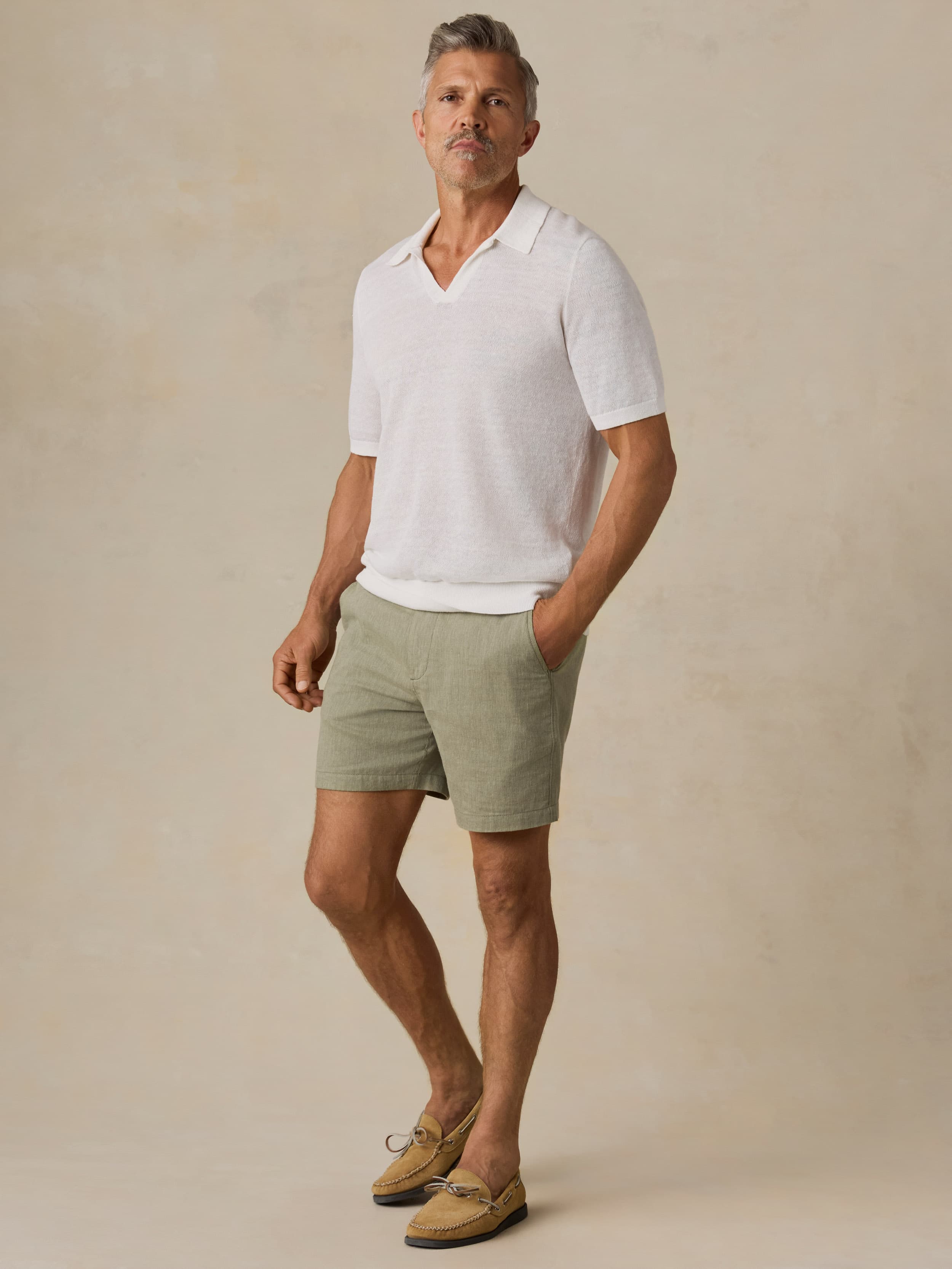 Man wearing a white polo shirt and green shorts against a beige background
