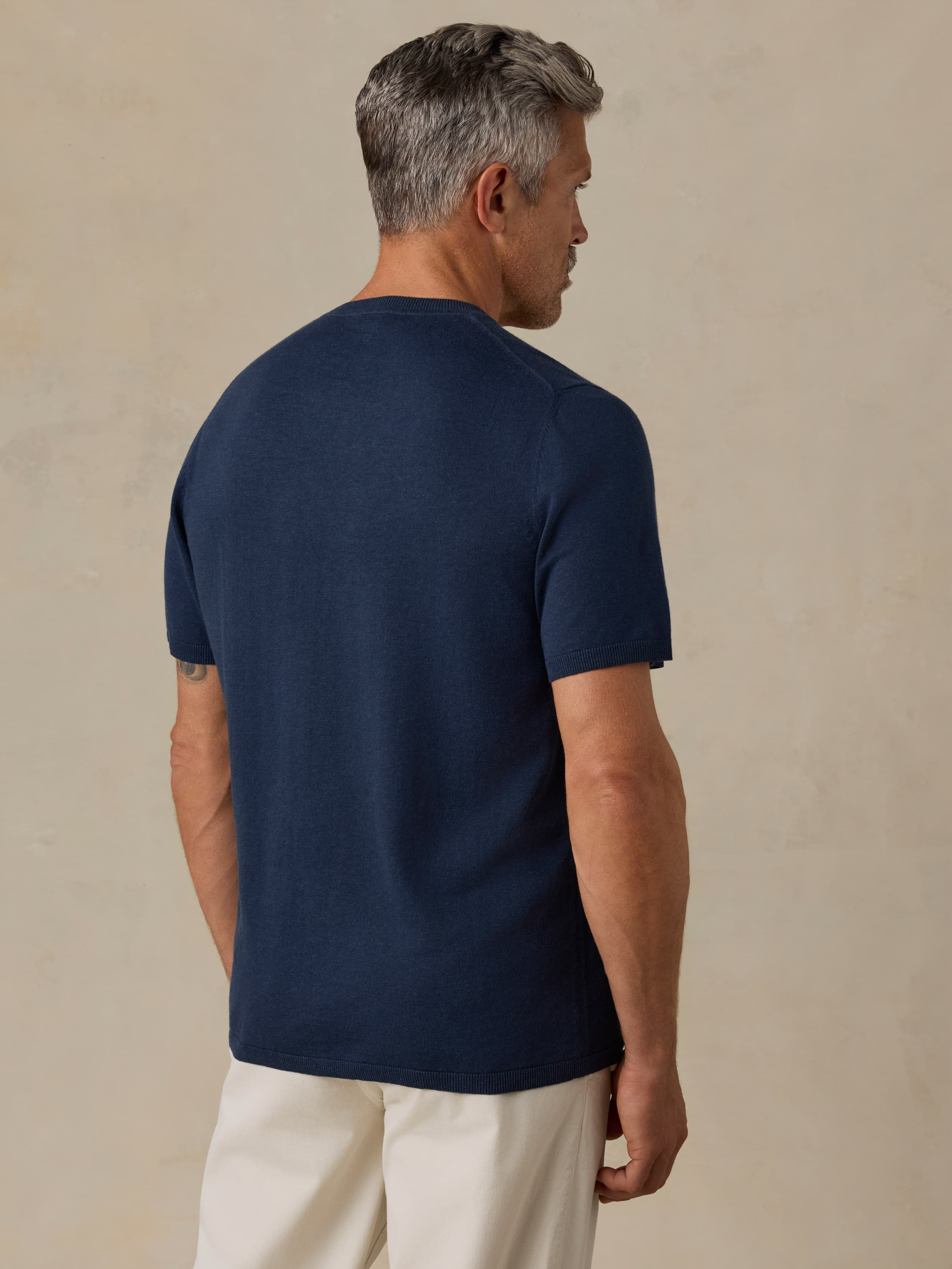 Man wearing a navy blue t-shirt and beige pants against a beige background