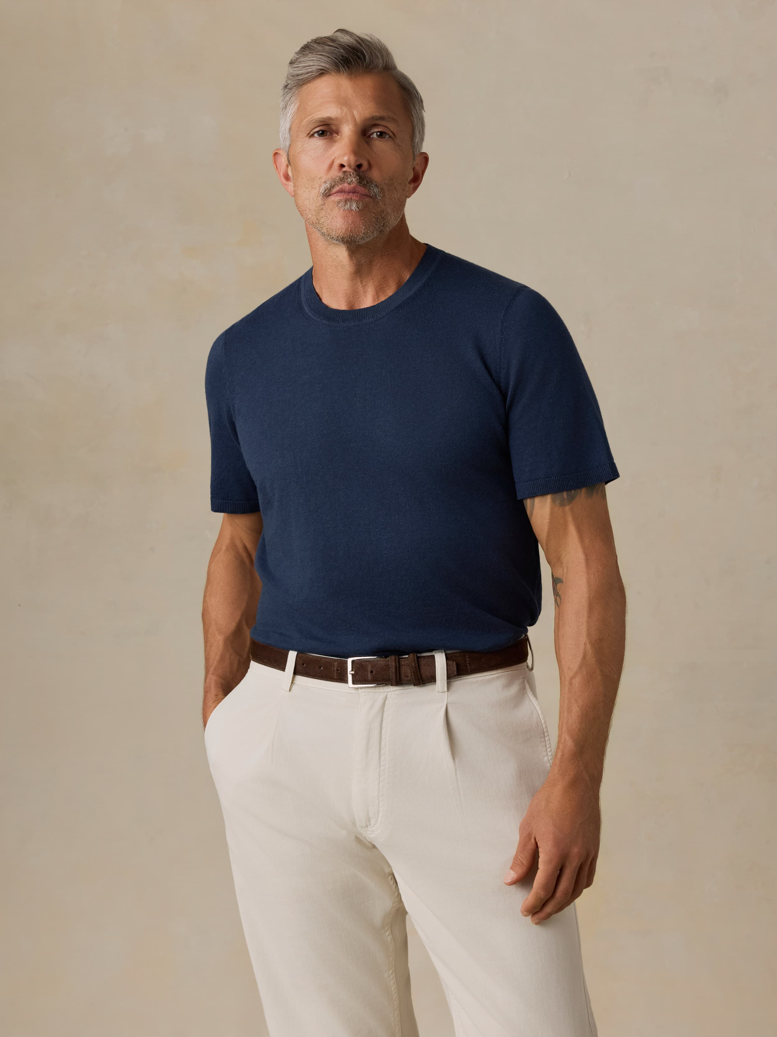 Man wearing a navy blue t-shirt and white pants against a beige background