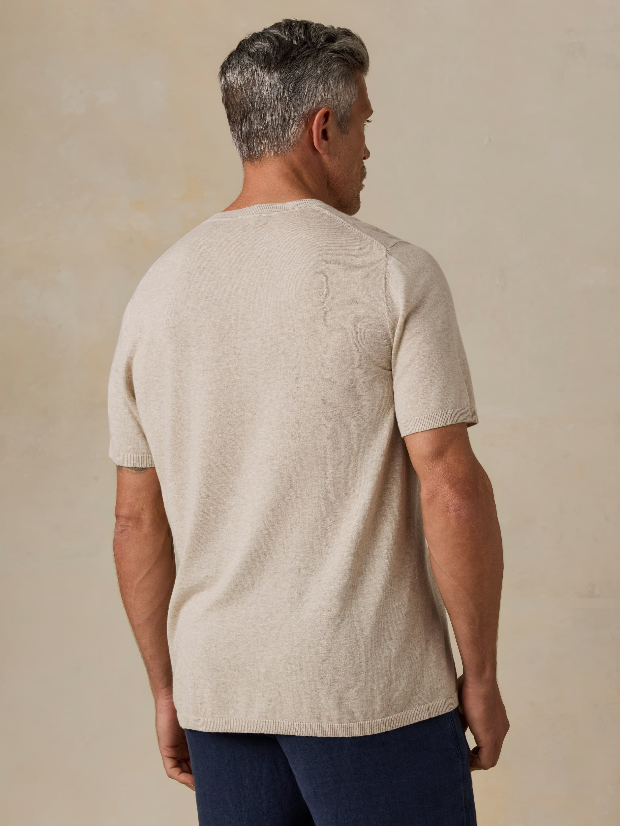 Man wearing a beige t-shirt and navy blue pants against a beige background
