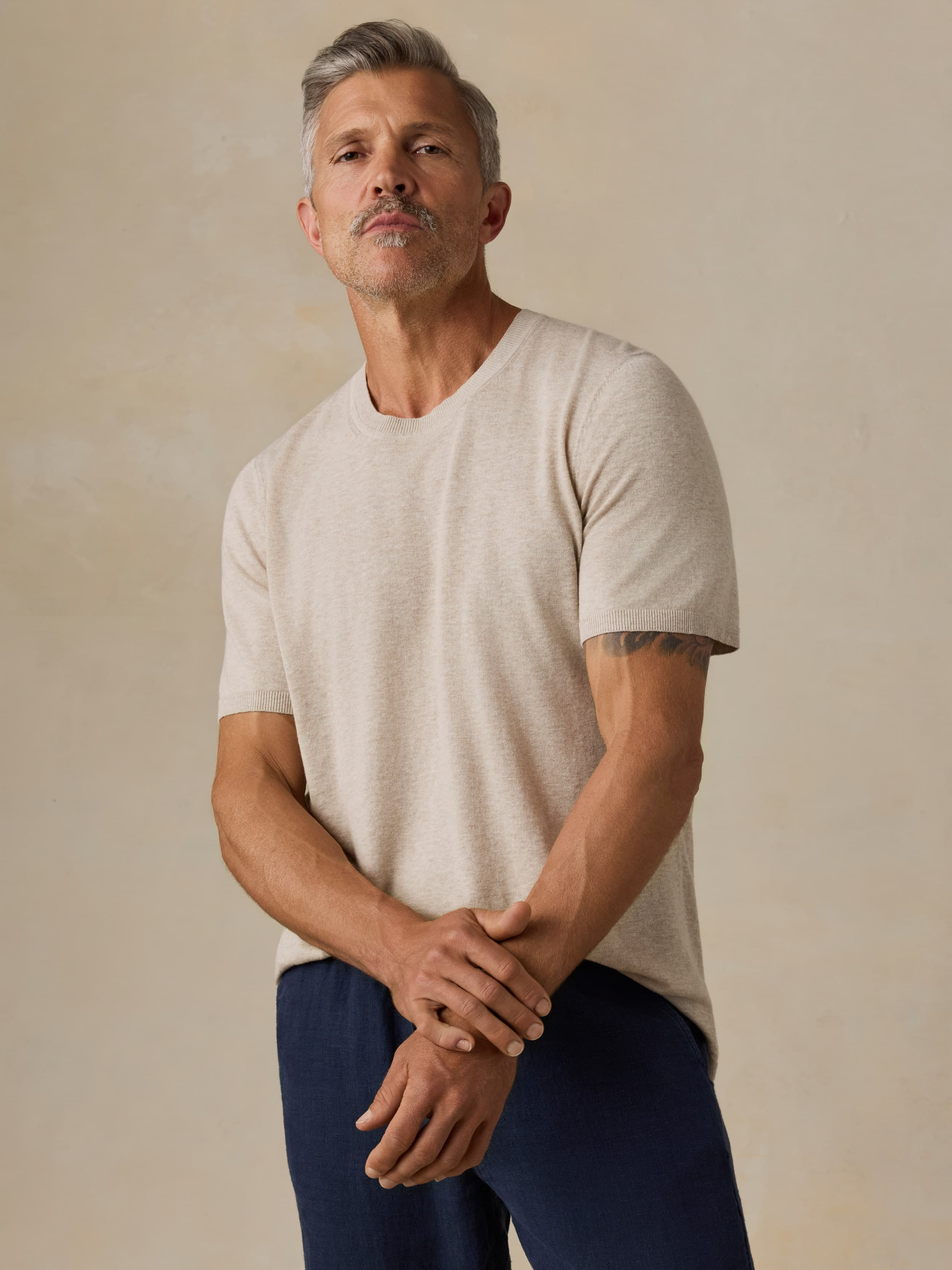 Man wearing a beige t-shirt and navy blue pants against a beige background