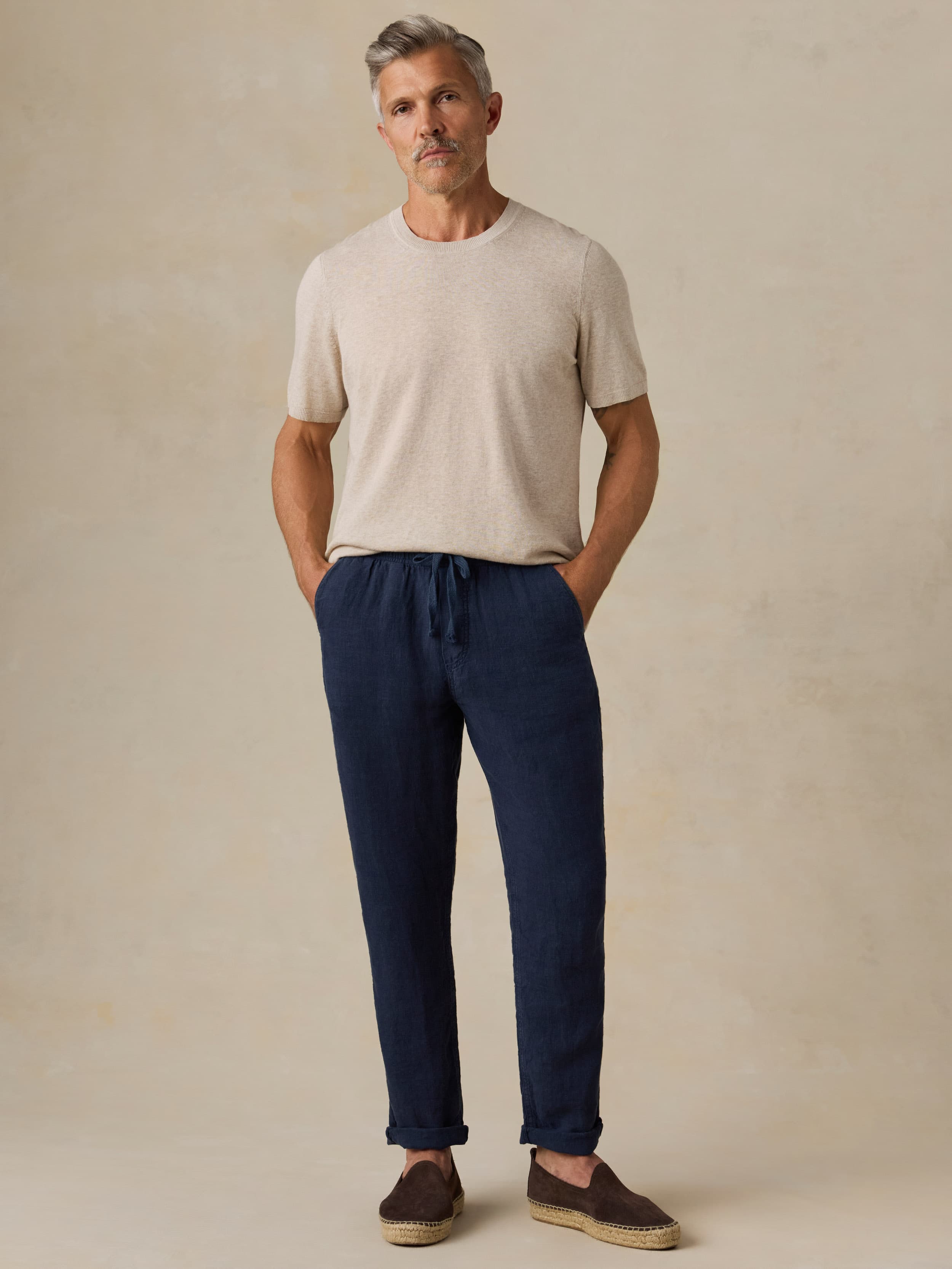 Man wearing a beige t-shirt and navy blue pants against a beige background