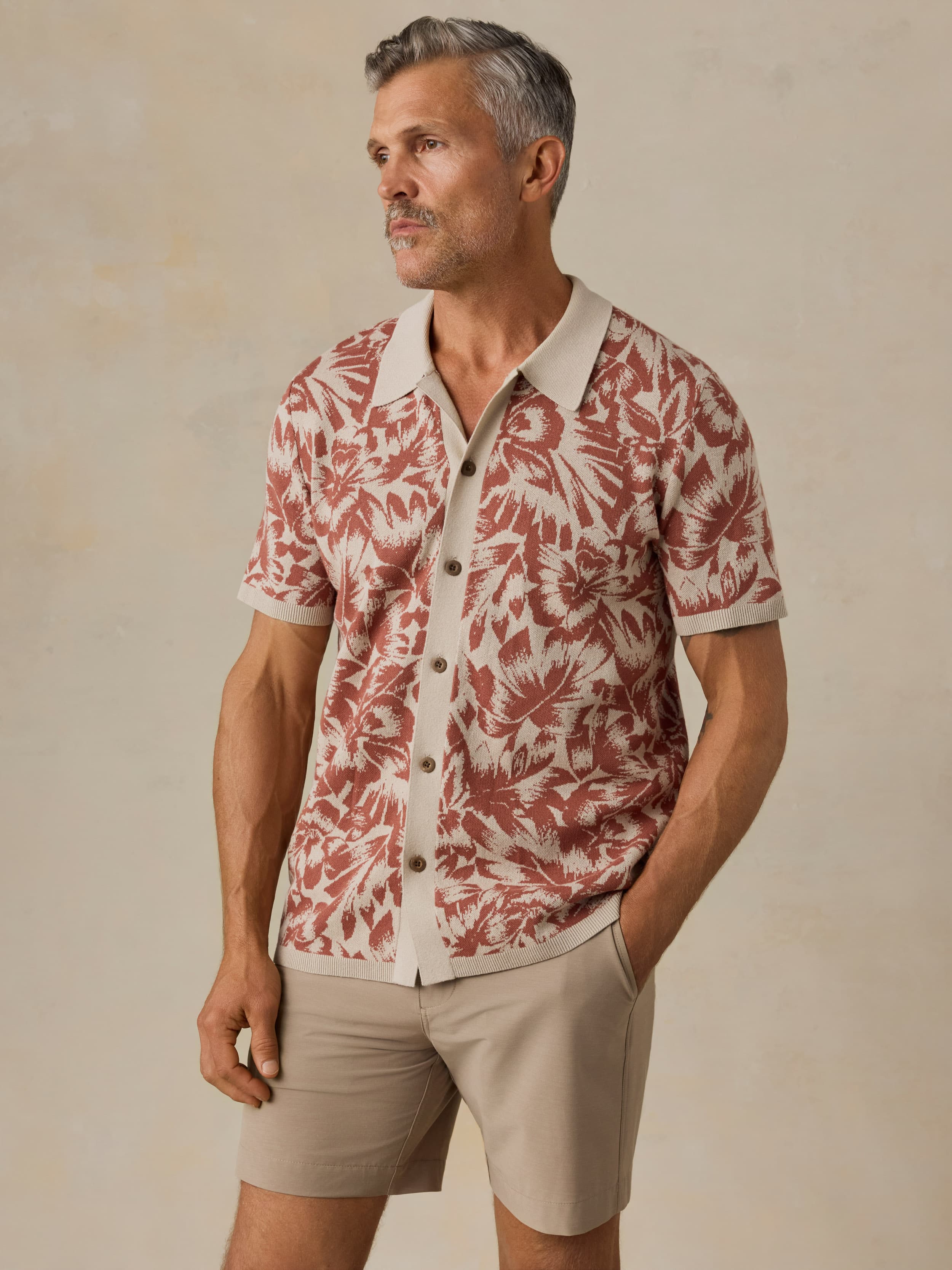 Man wearing a red and white floral patterned shirt with beige shorts against a beige background
