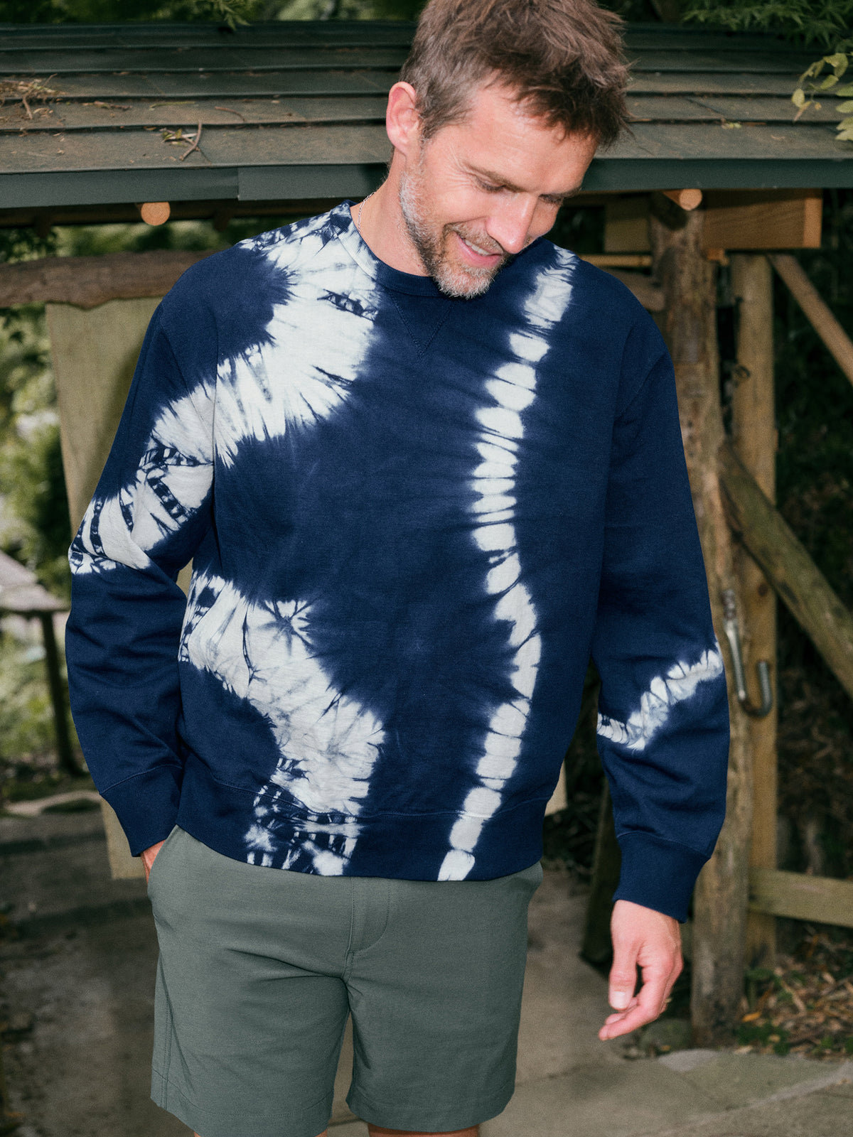 Man wearing a blue tie dye sweatshirt and green shorts, image 1 of 6