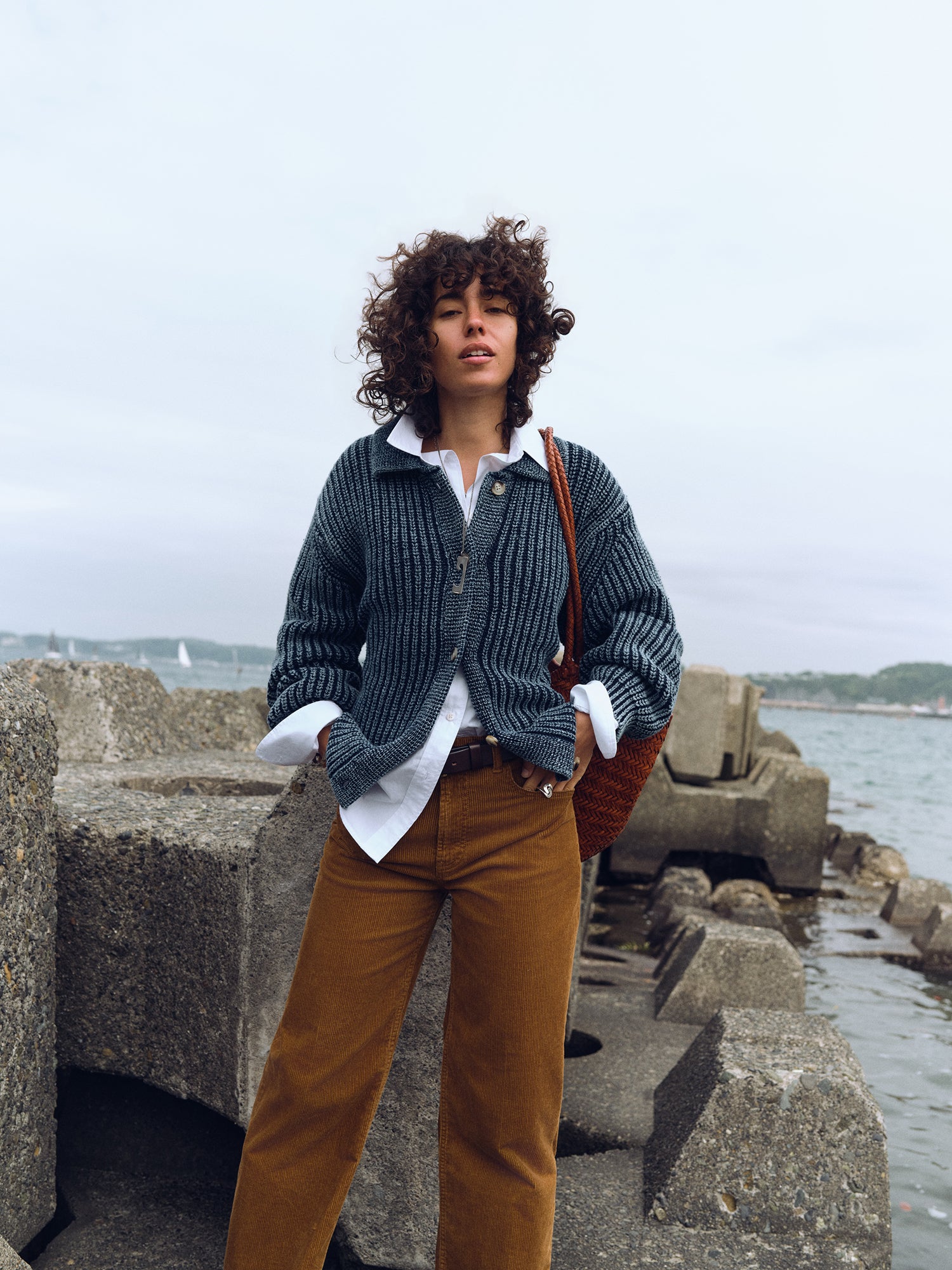 A woman wearing a blue sweater over a white button up shirt and tan corduroy pants