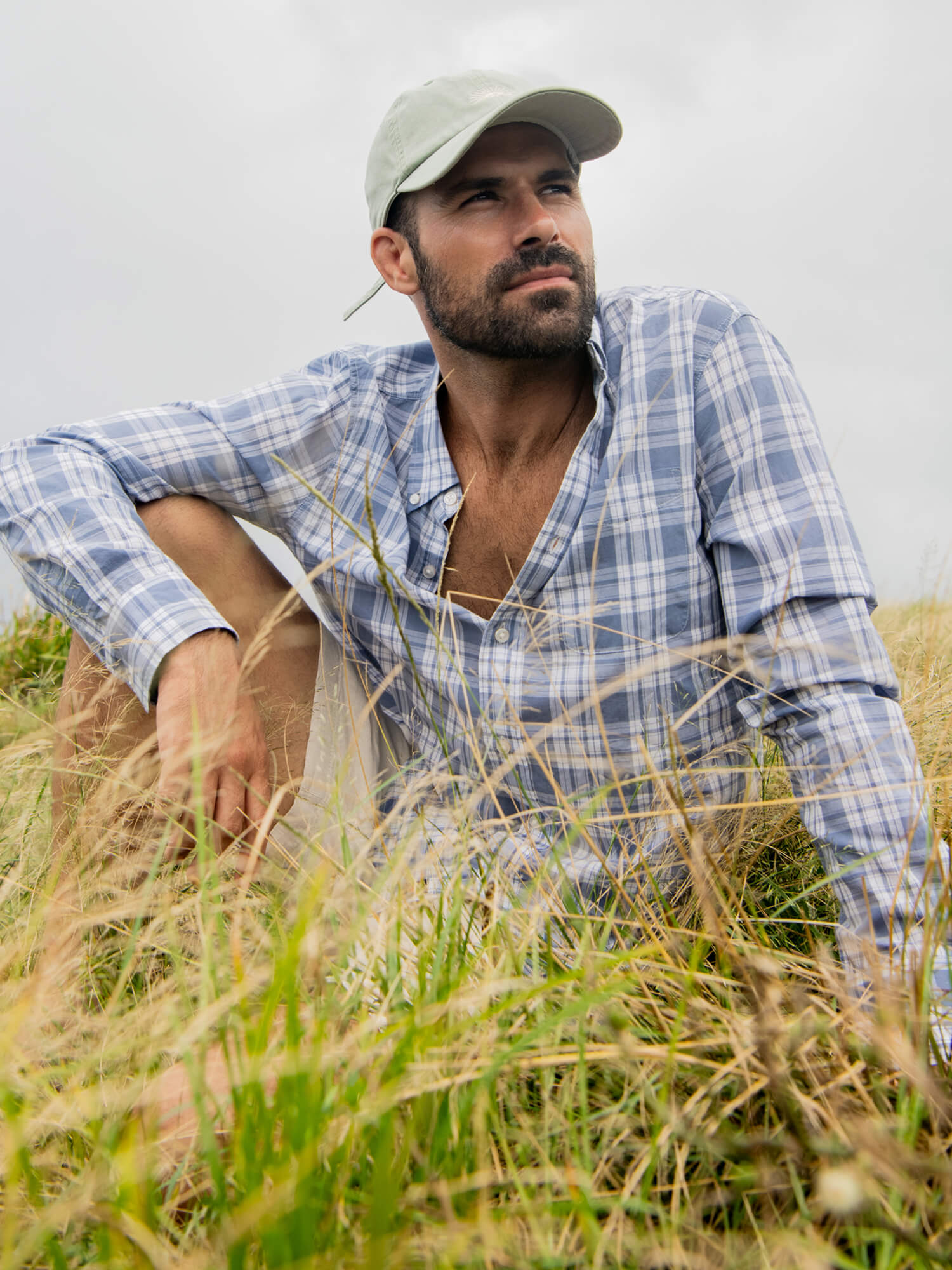 Man sitting in a field wearing a blue striped long sleeve shirt
