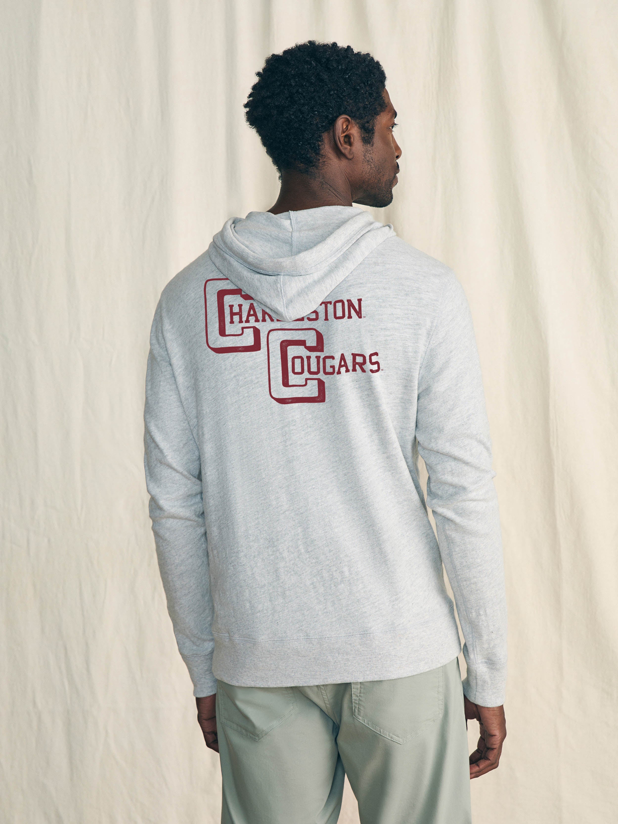 Man is wearing a grey hoodie with College of Charleston graphic on the center back against a beige background