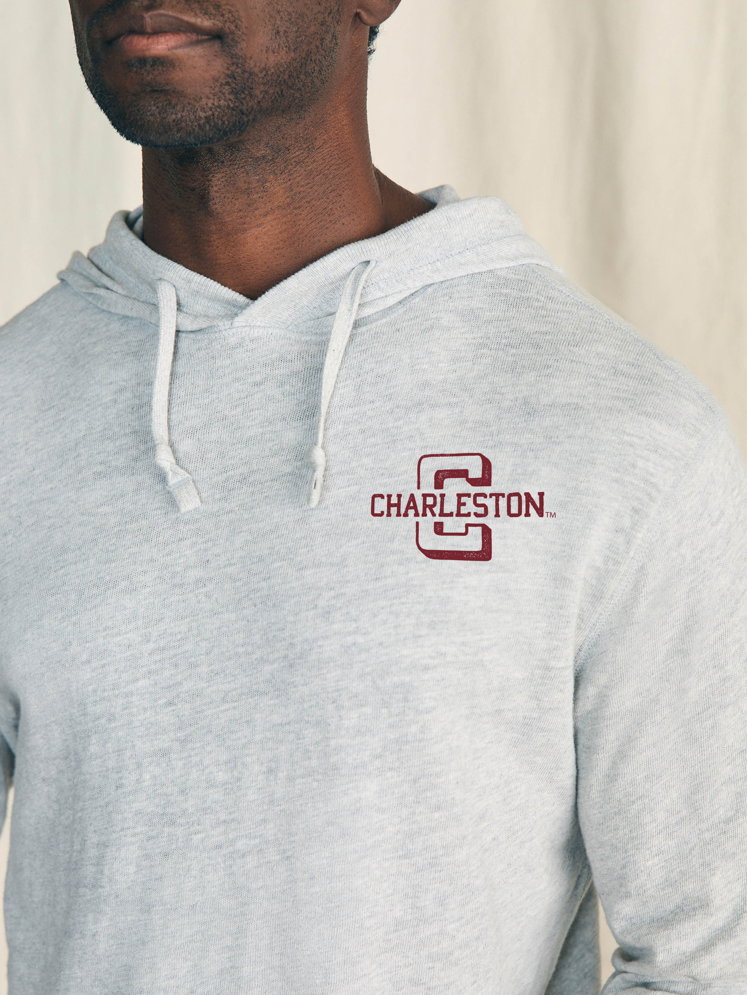 Man is wearing a grey hoodie with College of Charleston graphic on the left chest against a beige background