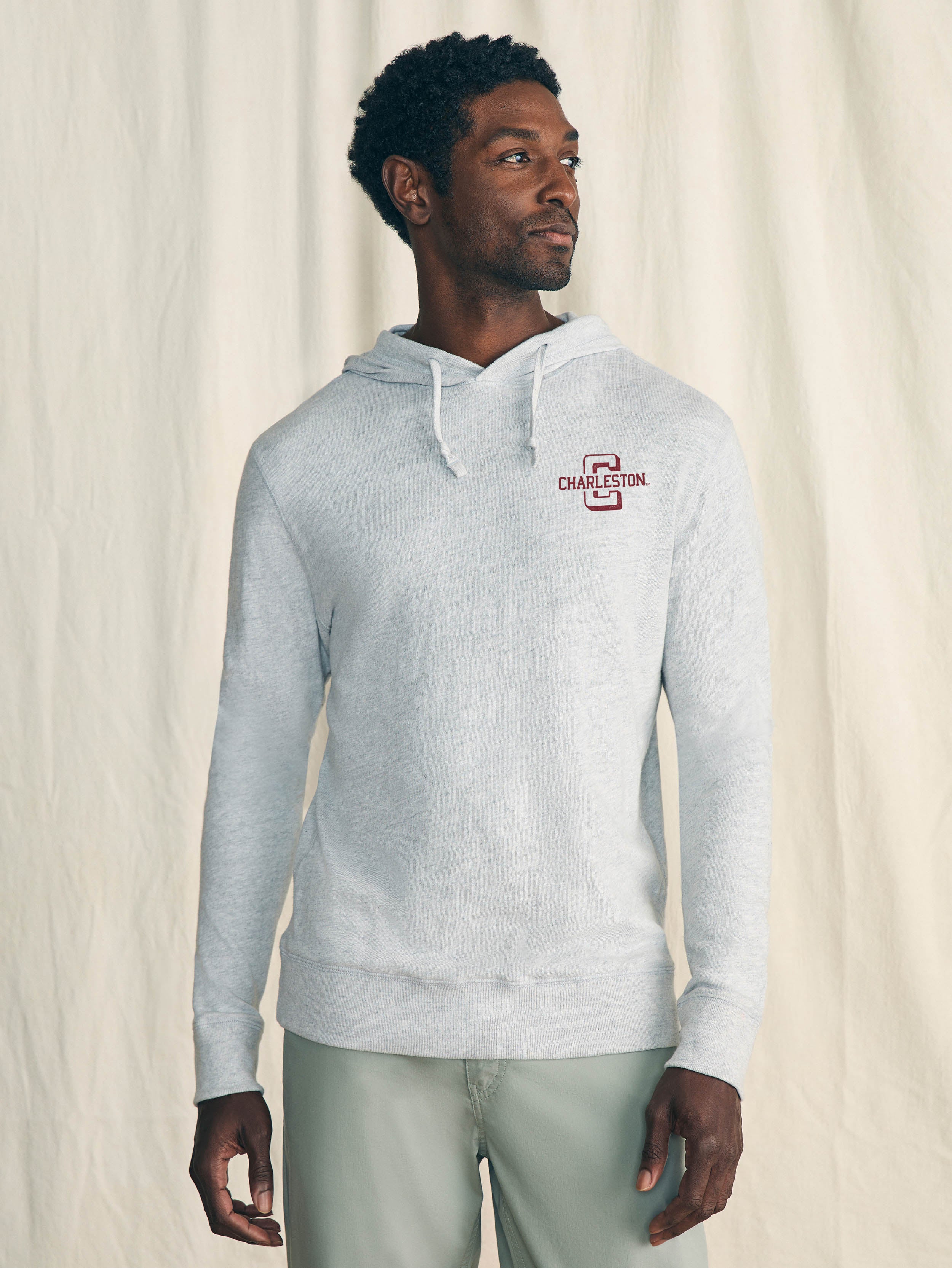 Man is wearing a grey hoodie with College of Charleston graphic on the left chest against a beige background