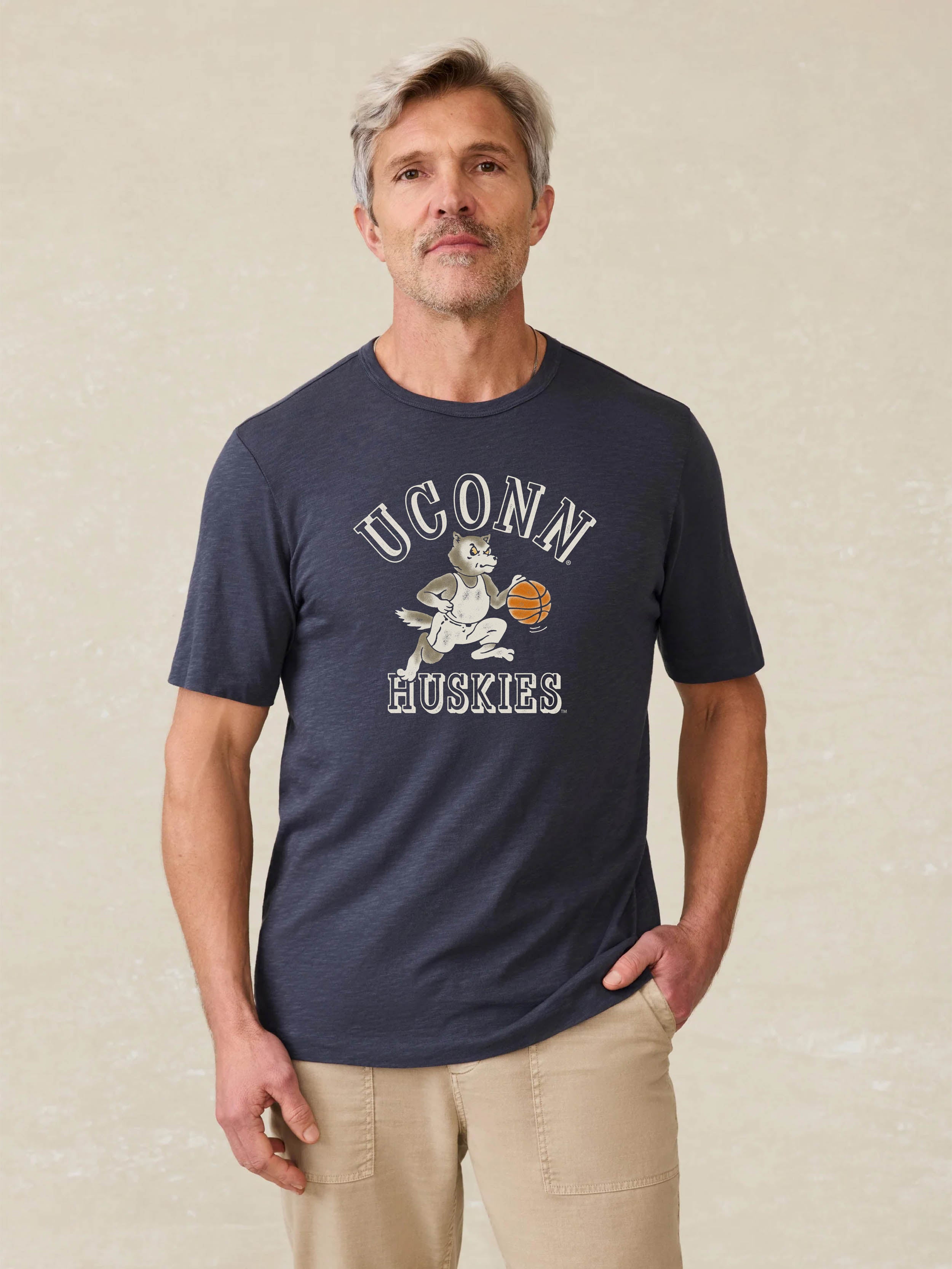 Man wearing a navy blue t-shirt with UConn Huskies graphic on the center front against a beige background