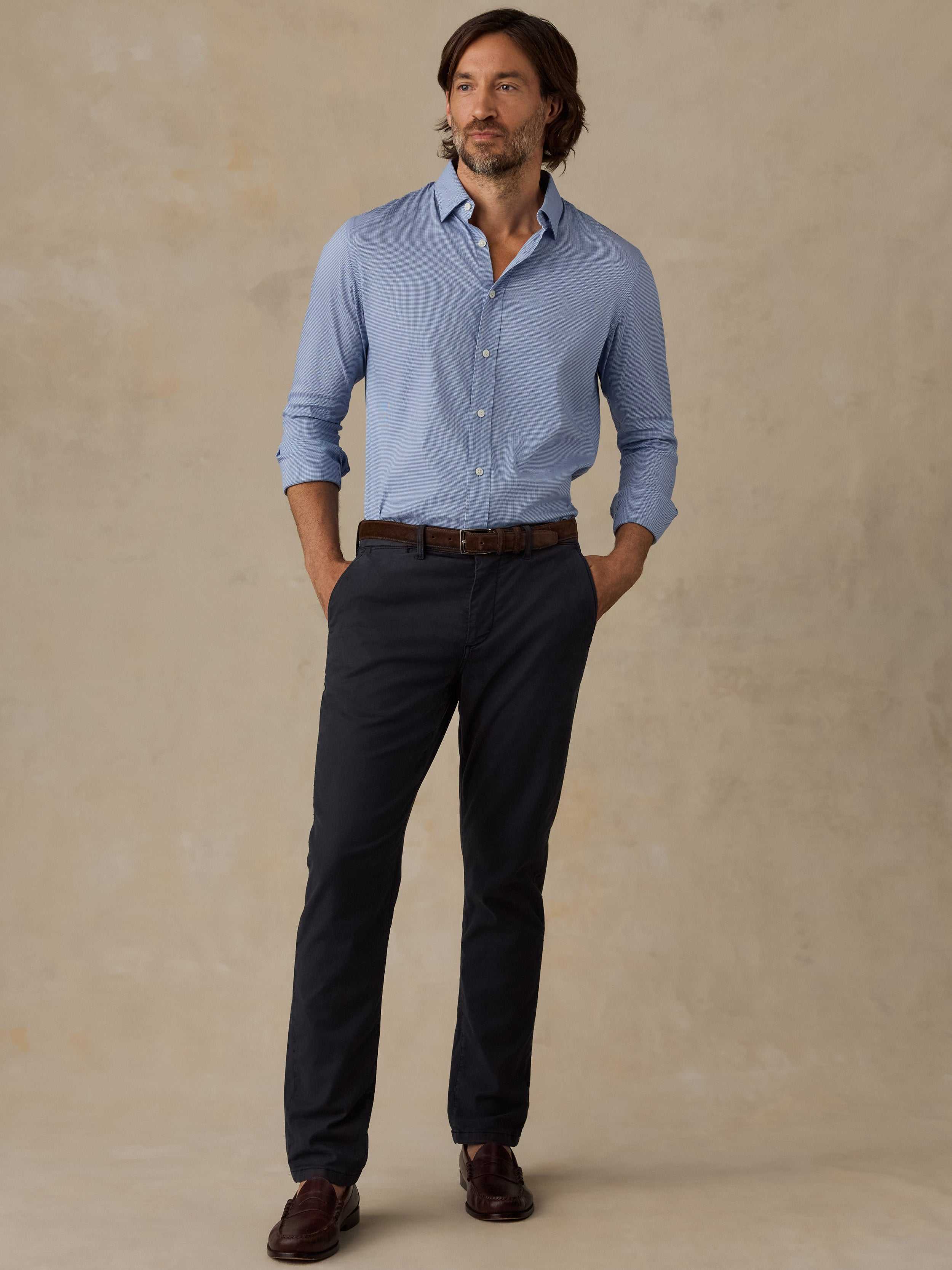 Man wearing a light blue button-up shirt and navy chino pants against a beige background