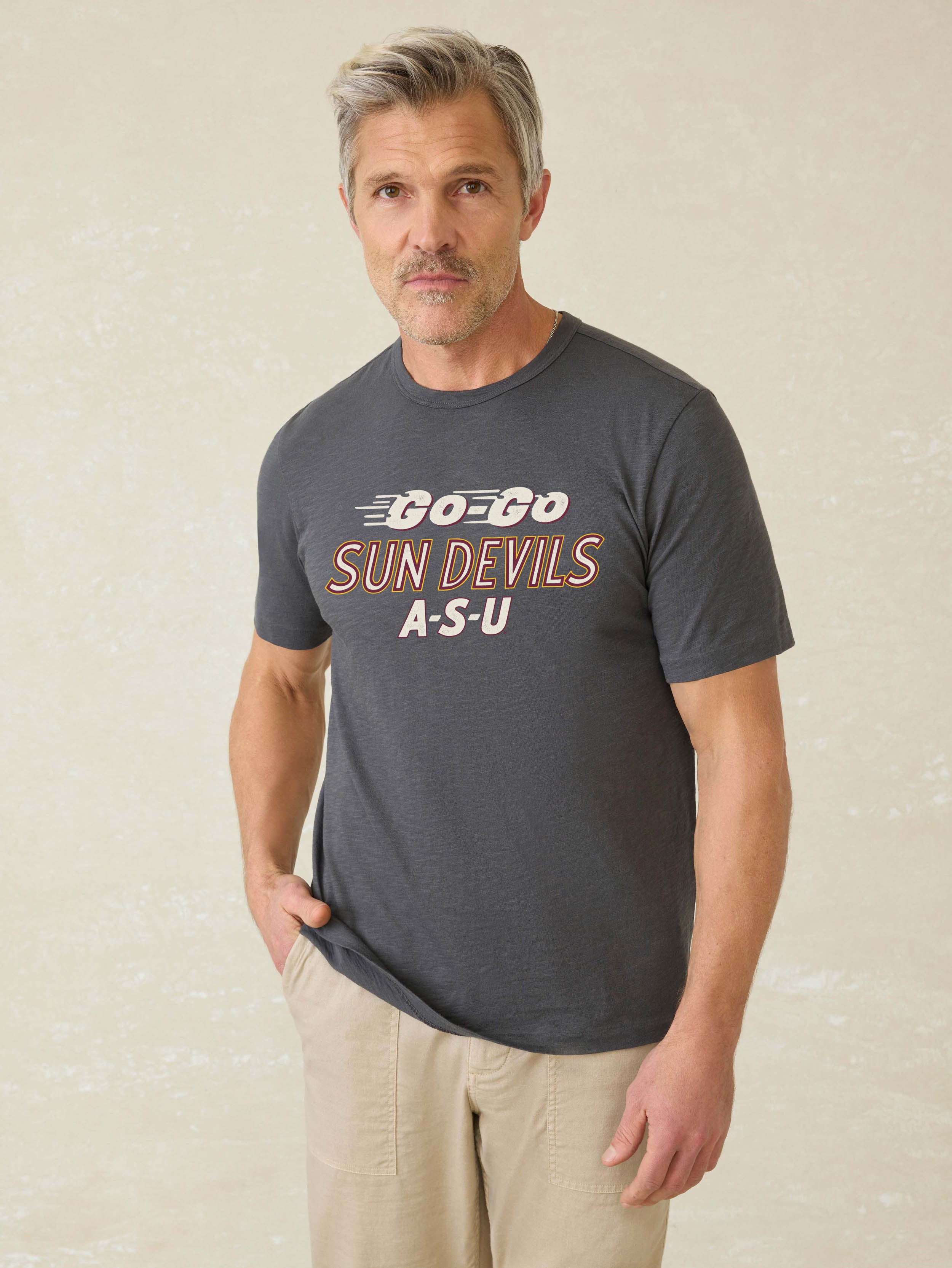 Man wearing a grey short sleeve t-shirt with Arizona State University graphic on the center front against a beige background