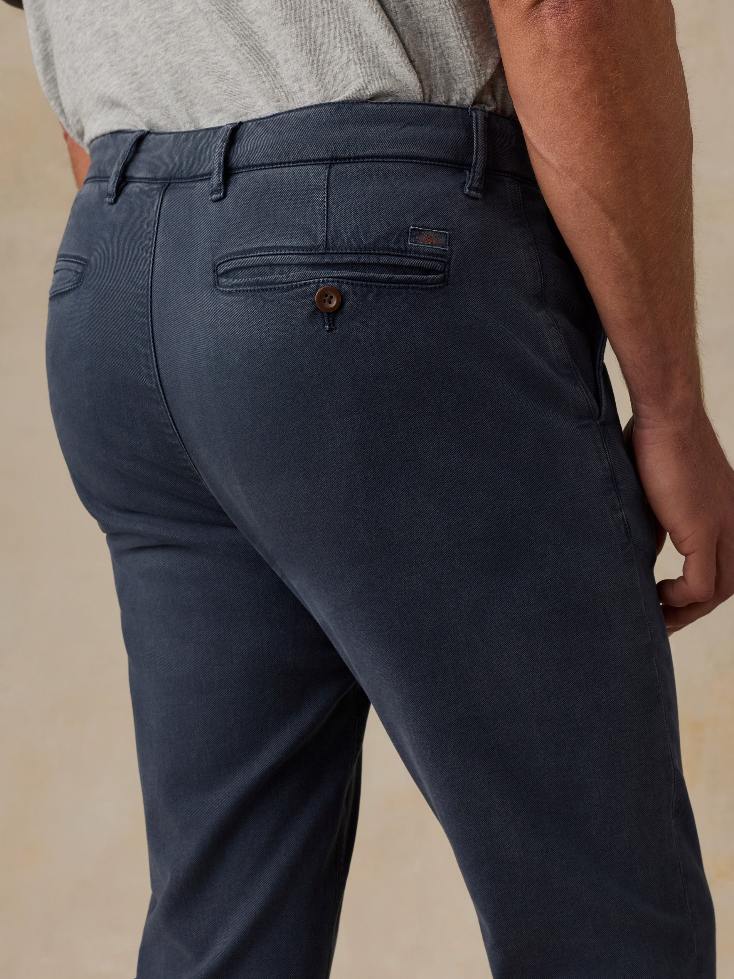 Close-up back view of a man wearing navy blue chino pants with a gray shirt, showing the waistband, belt loops, and back pocket details.