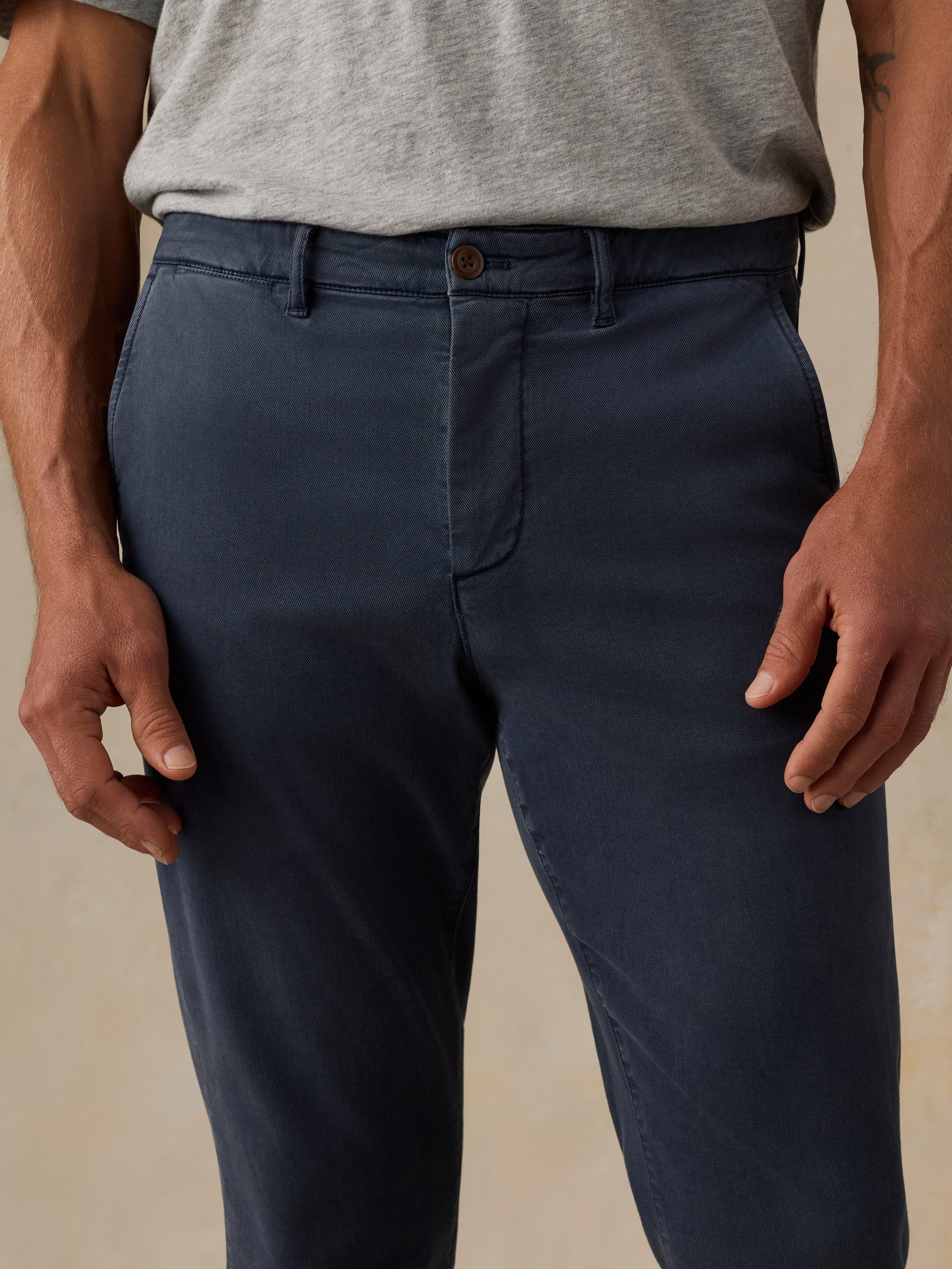 A close-up of a man wearing dark navy blue chinos with a gray t-shirt, showing the front waistband, belt loops, and front pockets.