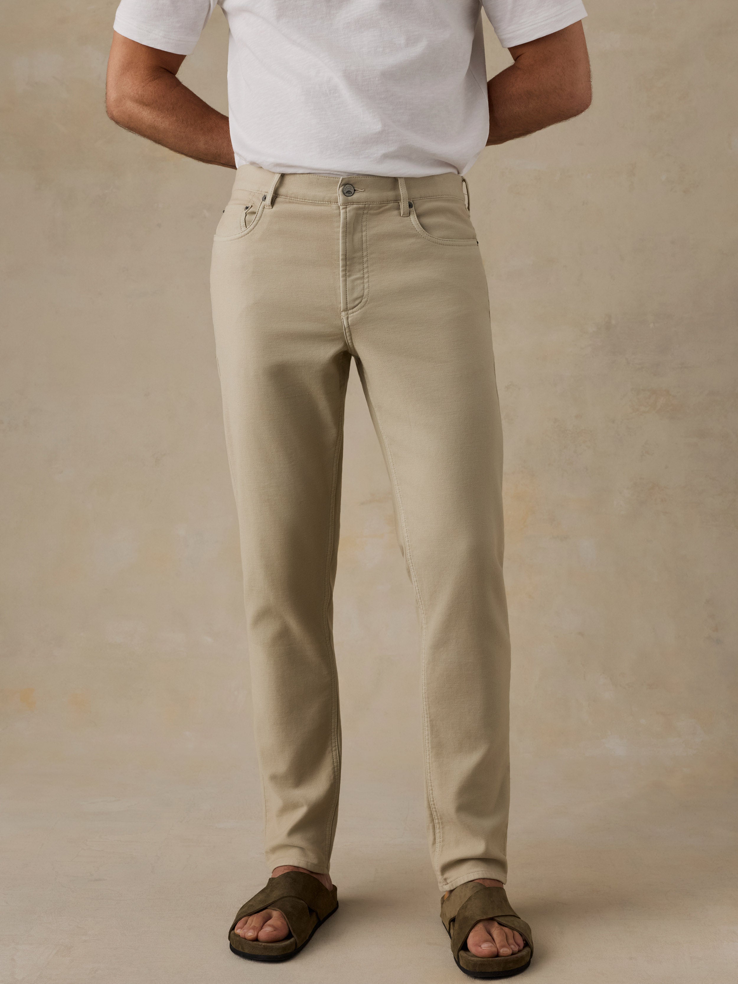 Man wearing light-colored pants and a blue plaid shirt against a beige background