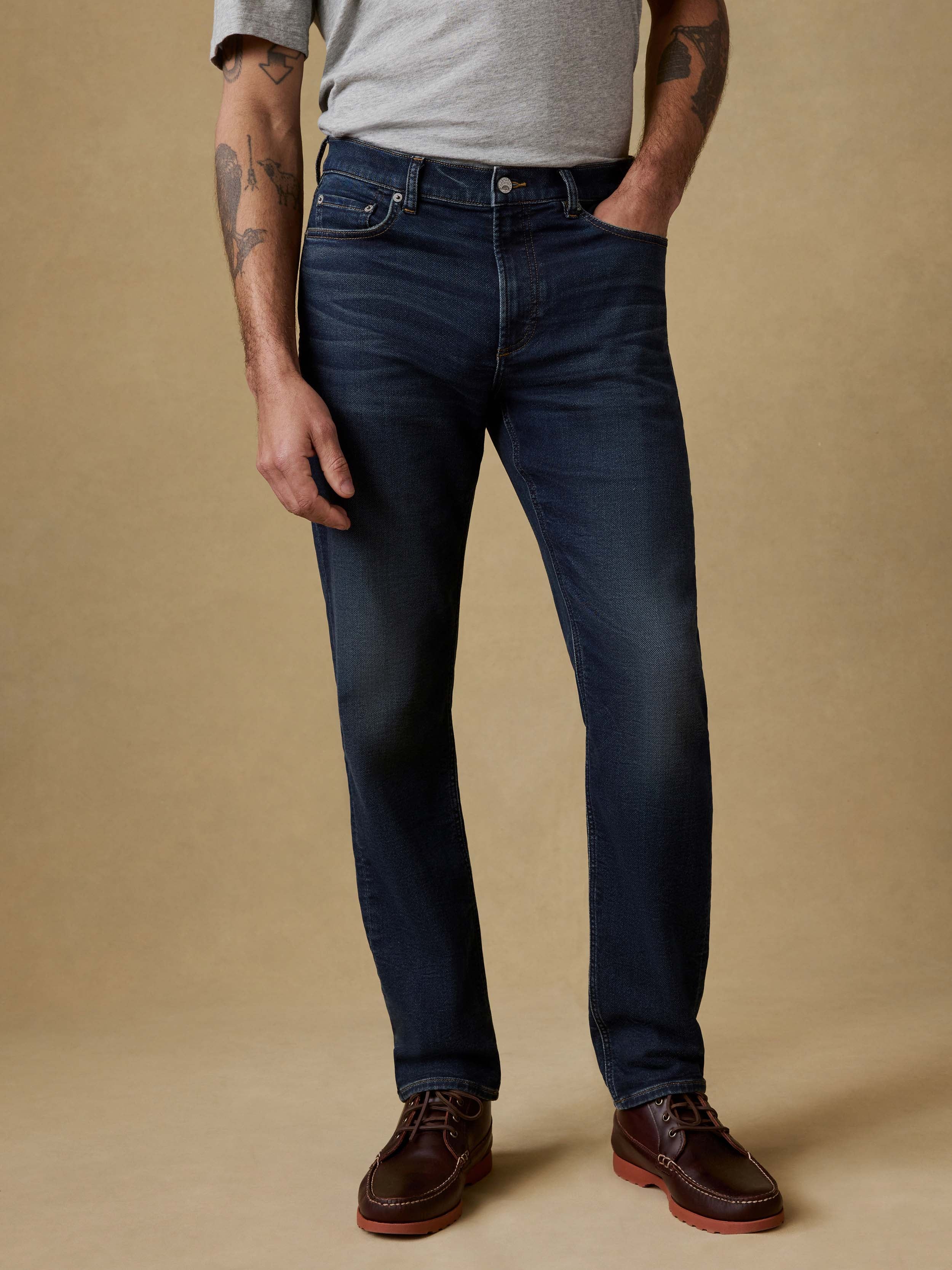 Man wearing a gray t-shirt and dark blue jeans against a beige background