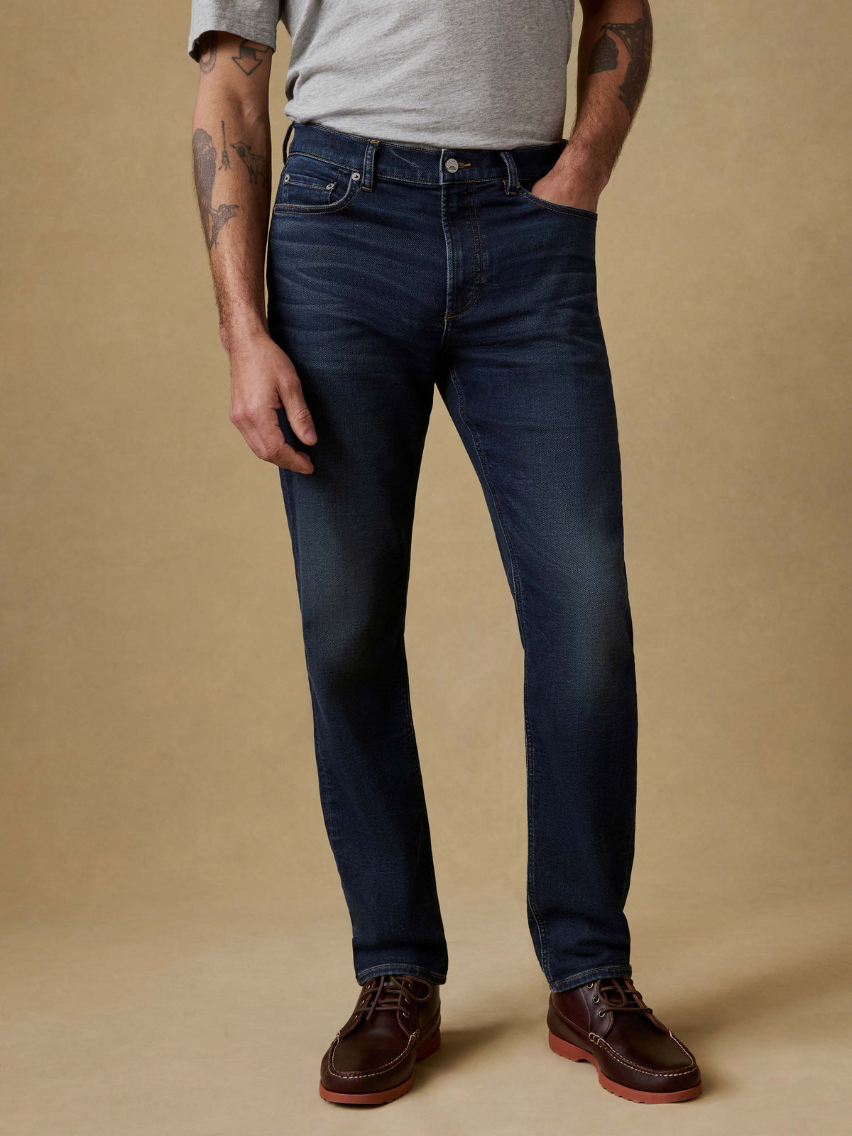 Man wearing a gray t-shirt and dark blue jeans against a beige background, image 1 of 6