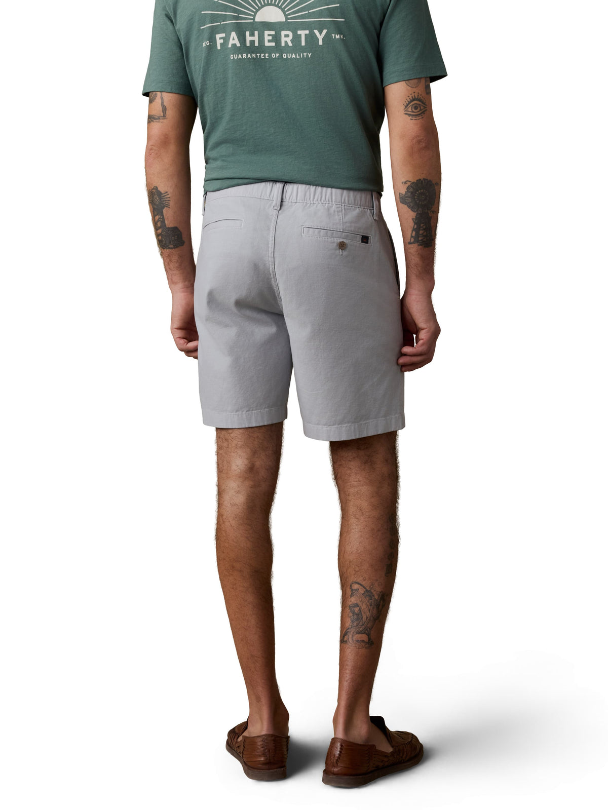A man viewed from behind wearing a green tee, grey shorts, and brown shoes, image 3 of 4