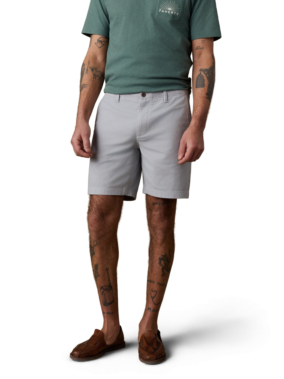 A man wearing a green tee, grey shorts, and brown shoes, image 2 of 4