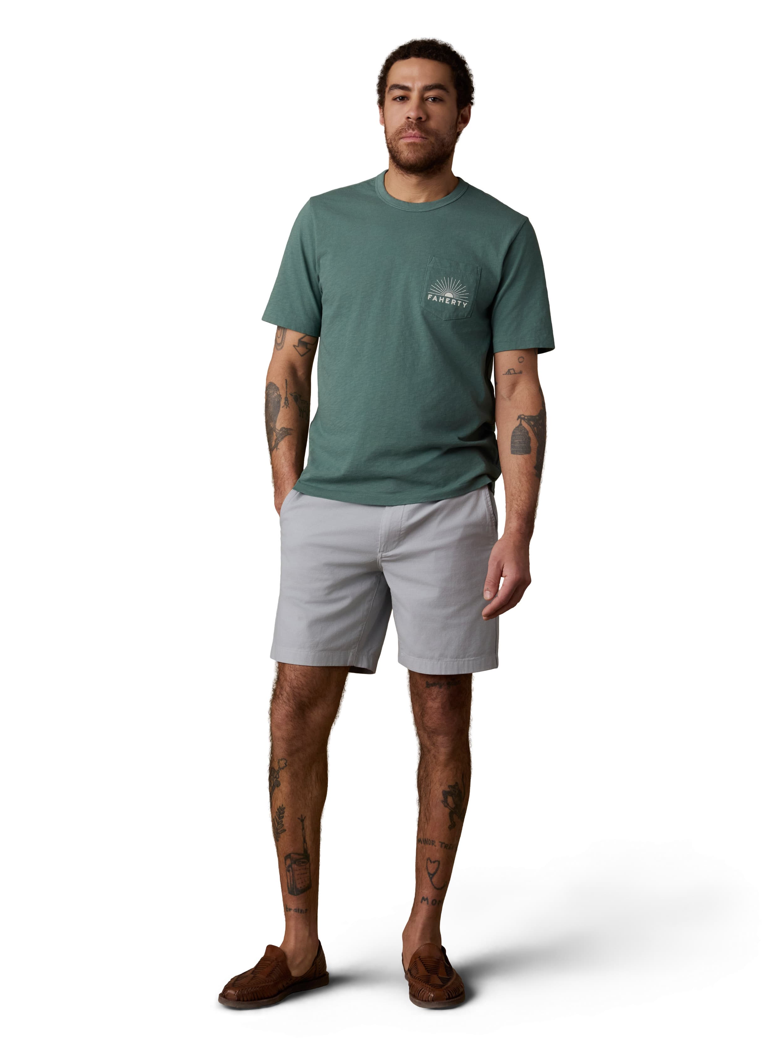 A man wearing a green tee, grey shorts, and brown shoes