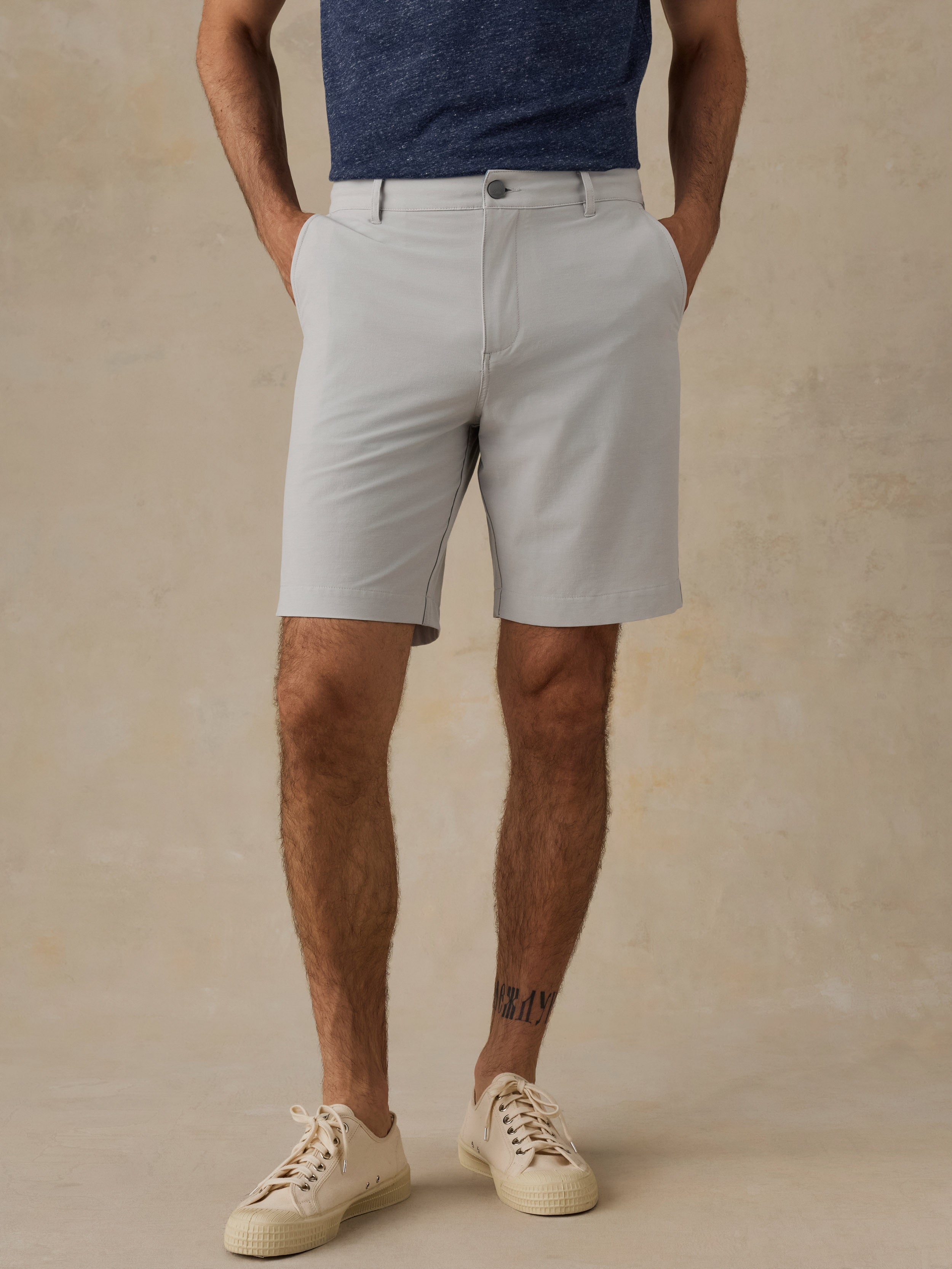 Man wearing light gray shorts and white sneakers on a beige background