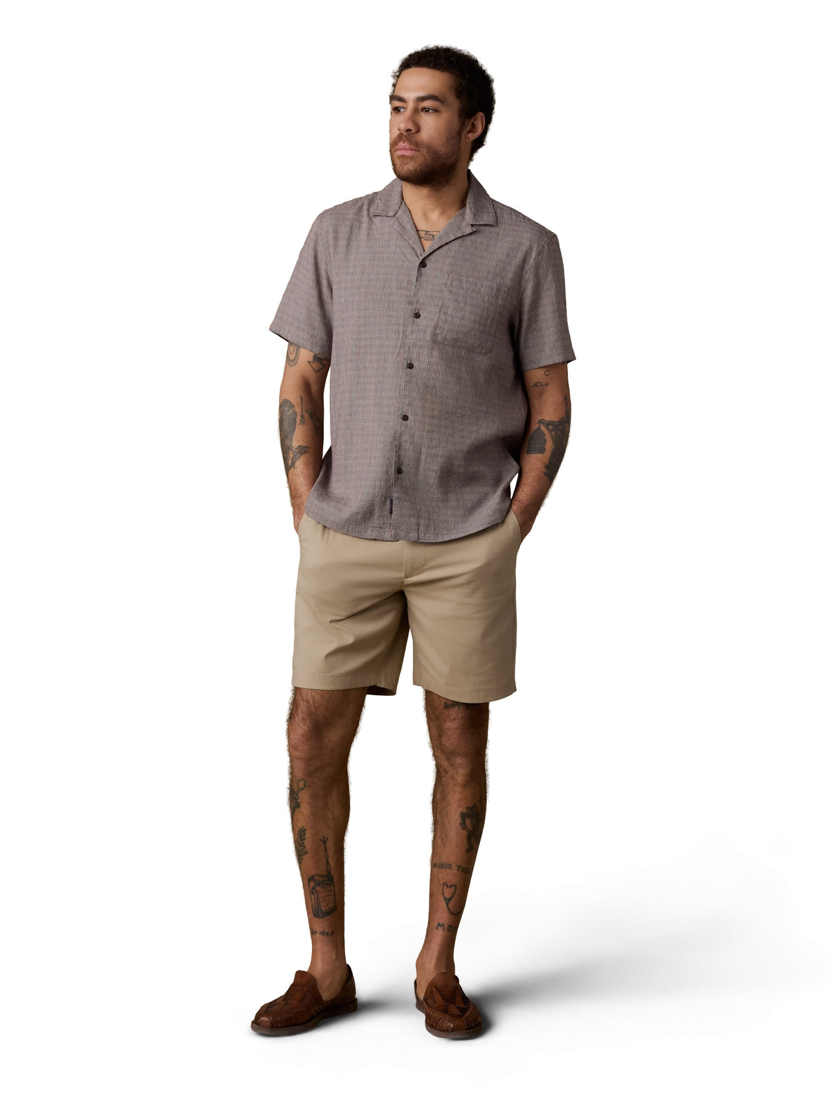 A man wearing a brown button up shirt, beige shorts, and brown shoes, image 1 of 3