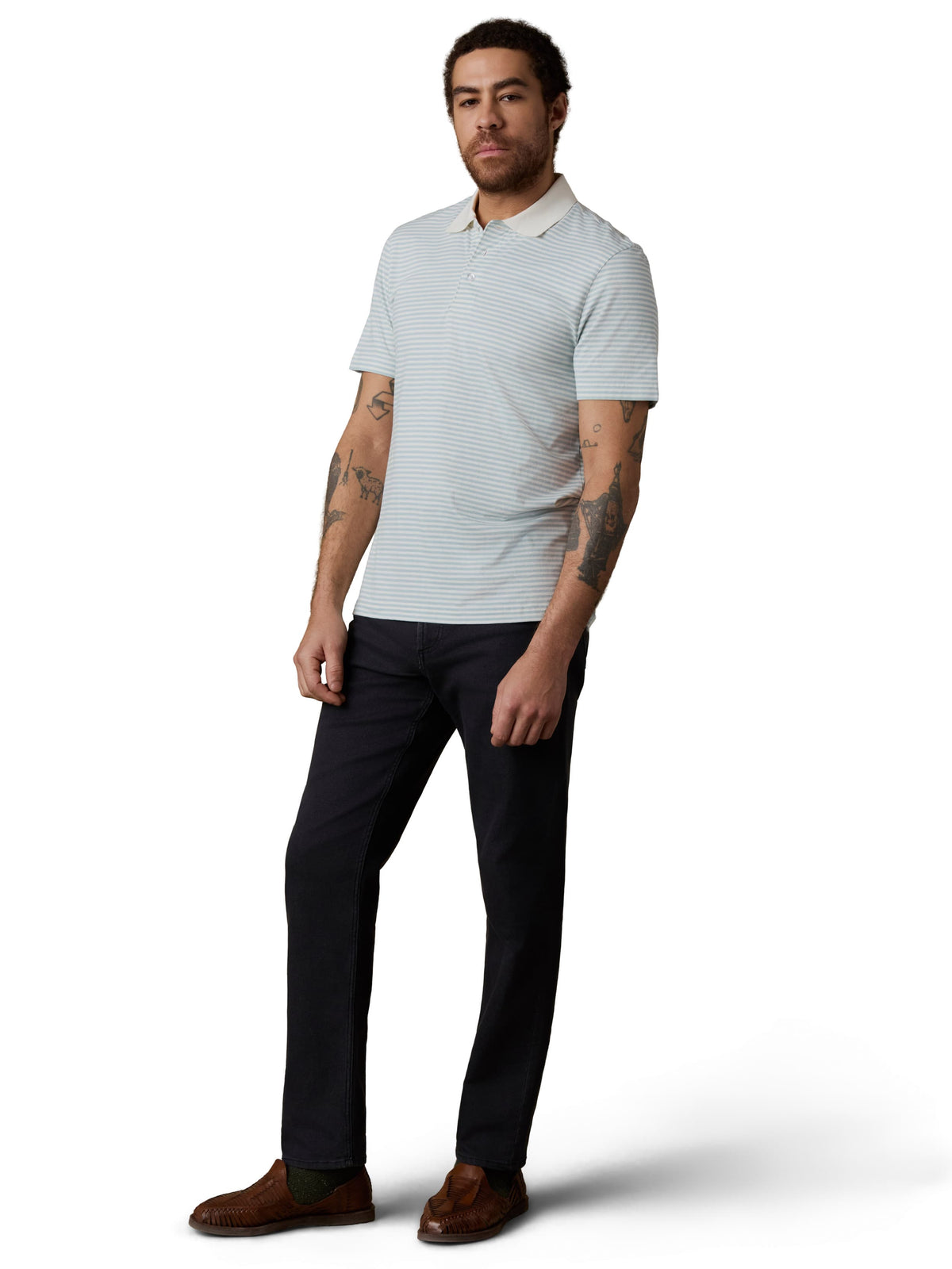 Man wearing a light blue striped polo shirt, dark jeans, and brown shoes, image 2 of 3