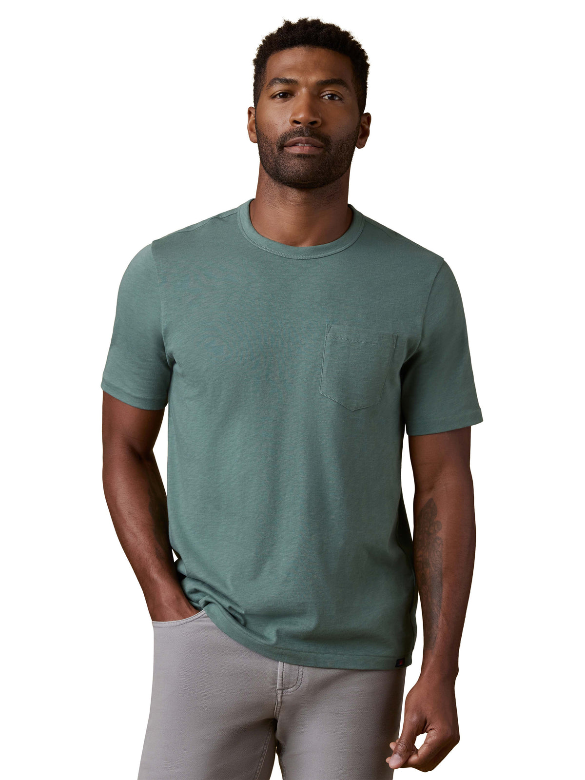 A man wearing a green tee and grey pants, image 1 of 3