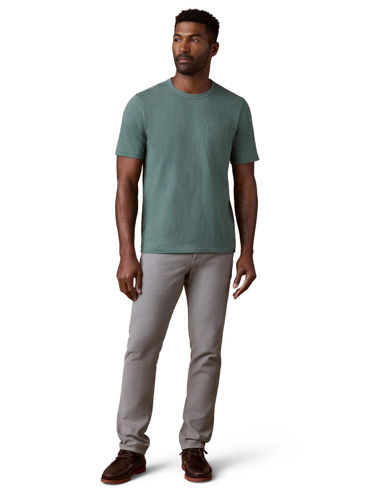 A man wearing a green tee, grey pants, and brown shoes, image 2 of 3