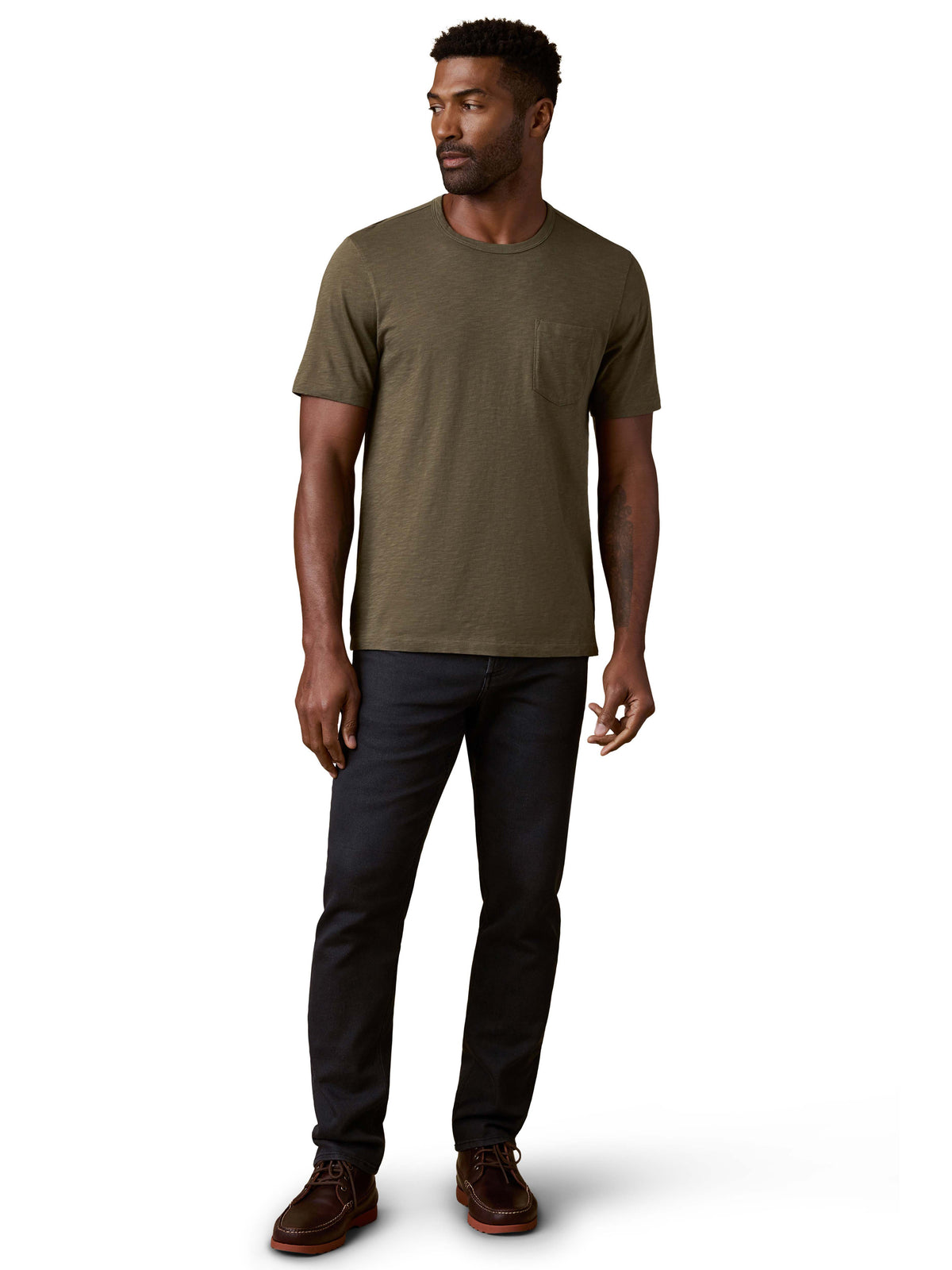 A man wearing a green tee, black jeans, and brown shoes, image 2 of 3