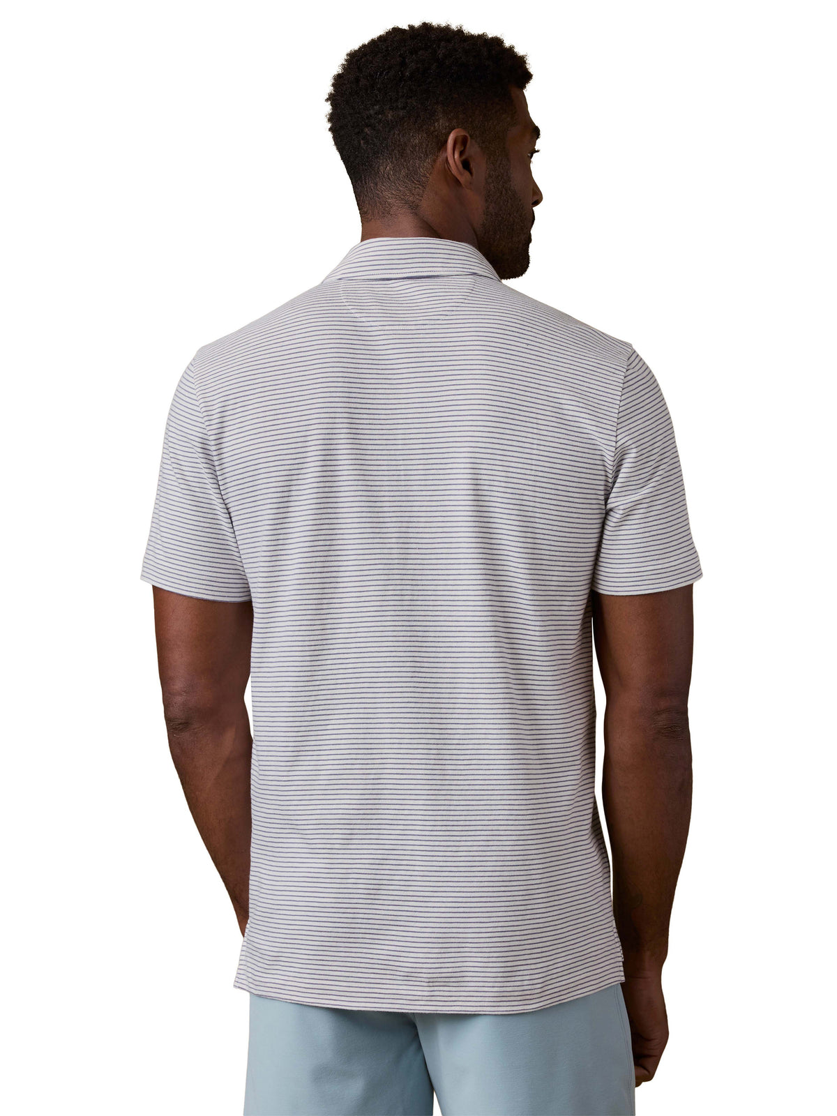 A man viewed from behind wearing a striped polo shirt and blue shorts, image 3 of 3
