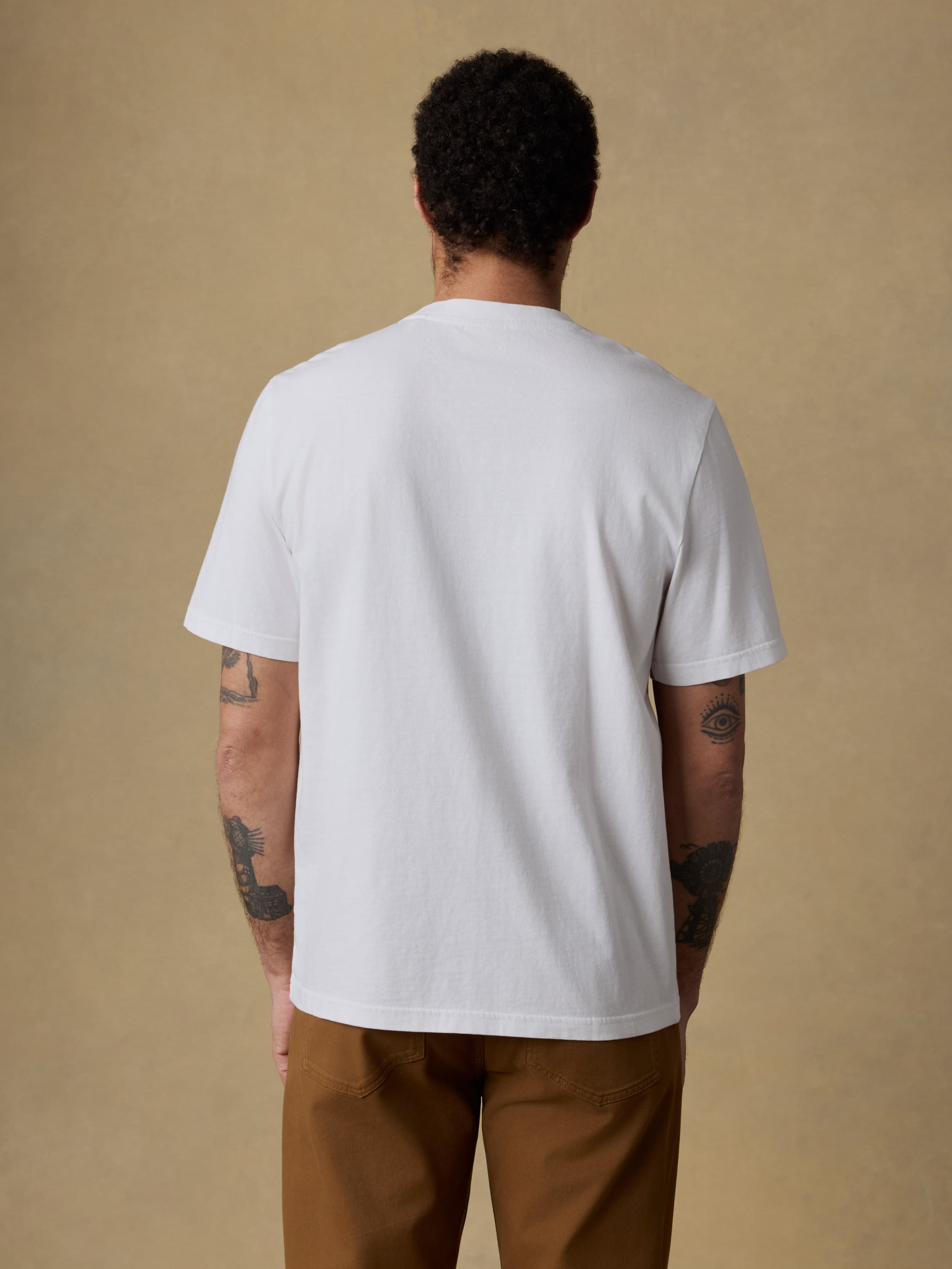 Man wearing a white t-shirt and brown pants against a beige background