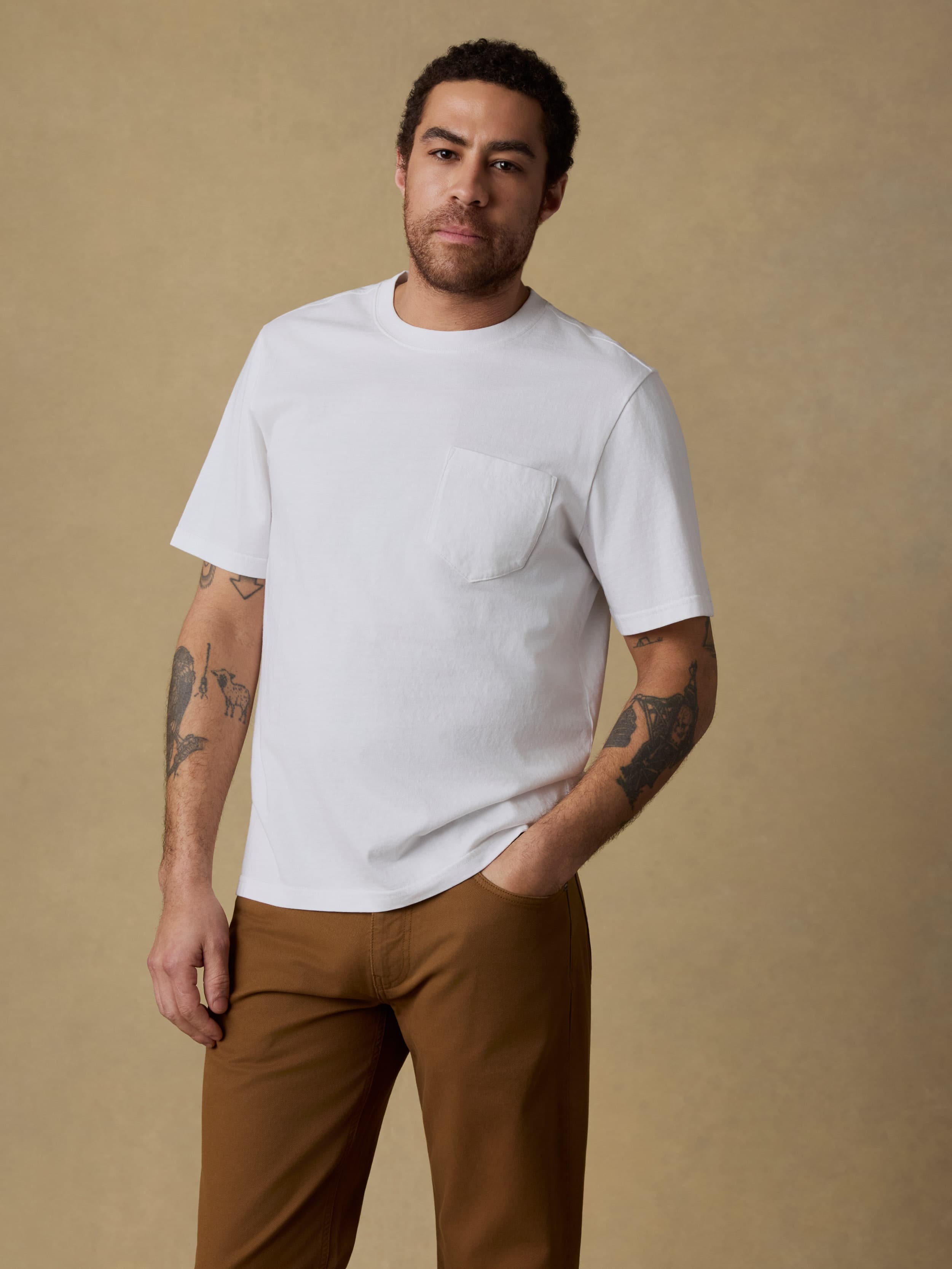 Man wearing a white t-shirt and brown pants against a beige background
