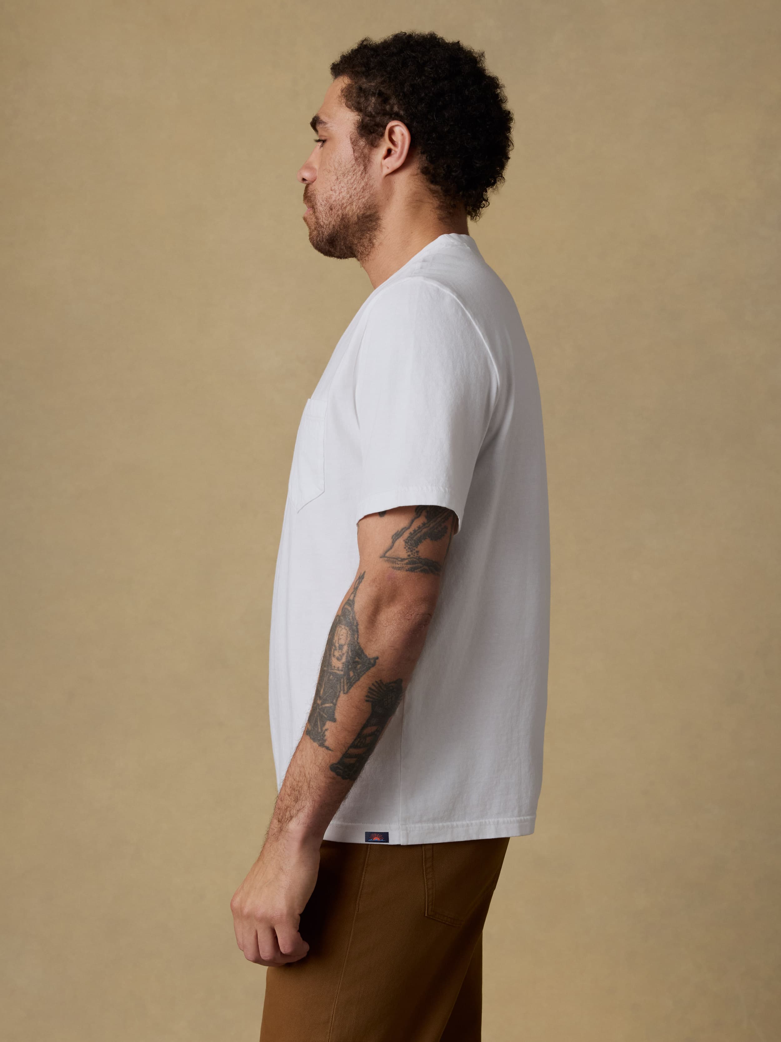 Man wearing a white t-shirt and brown pants against a beige background