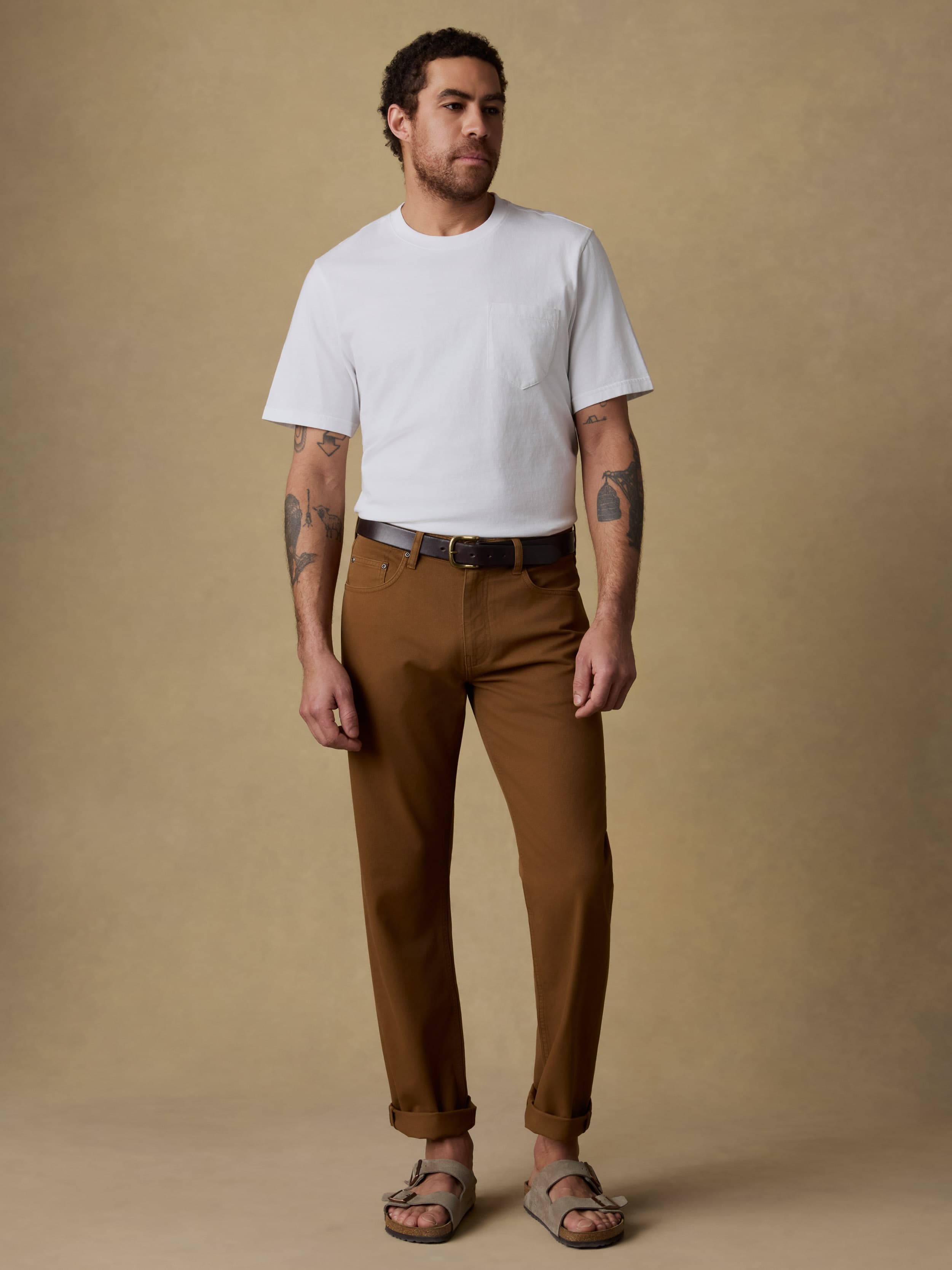 Man wearing a white t-shirt and brown pants against a beige background