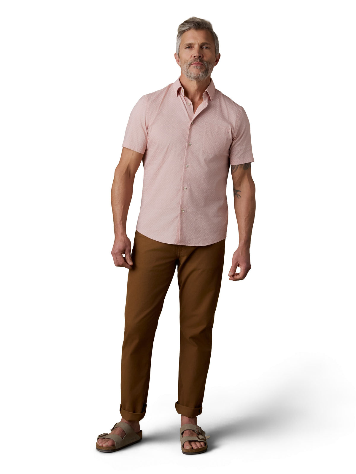 A man wearing a pink button up shirt, brown pants, and birkenstocks, image 2 of 3
