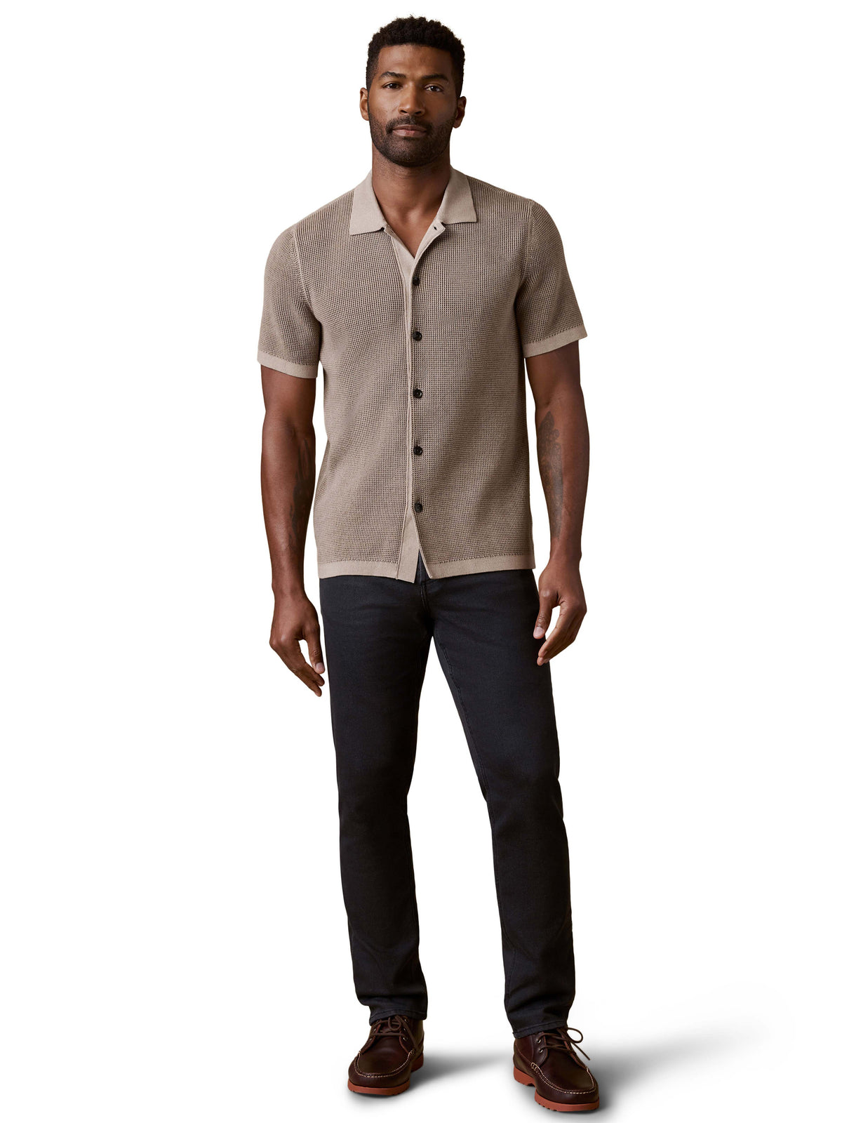 A man wearing a brown polo, dark jeans, and brown shoes, image 2 of 3