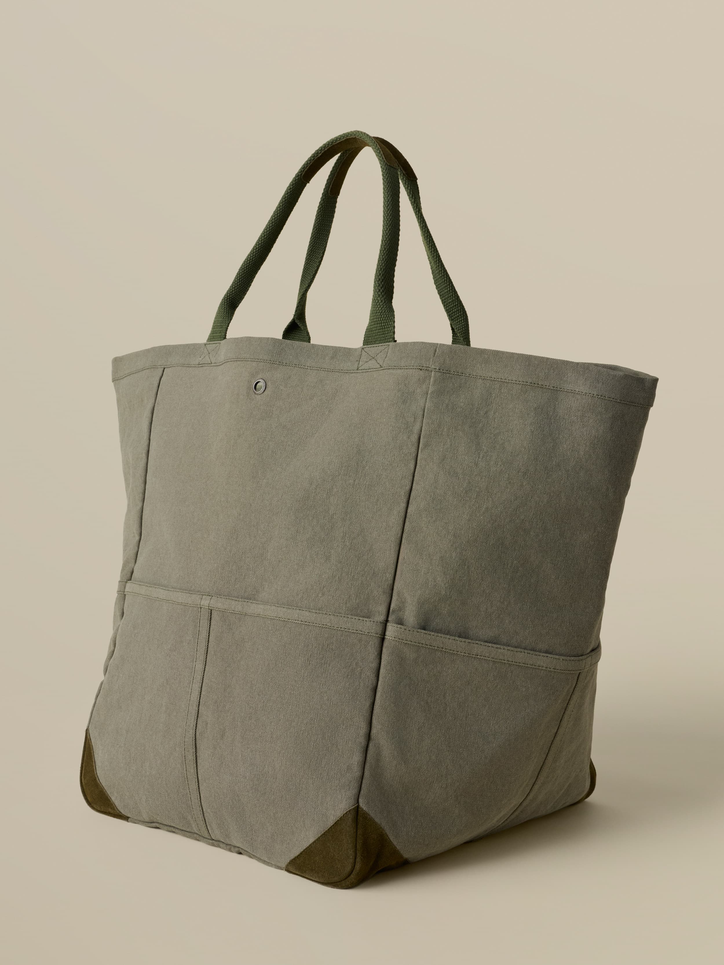 green tote bag with green suede accents against a beige background